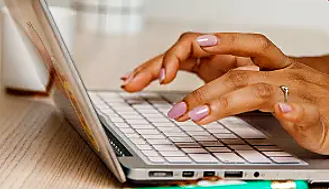 Hands with purple nail polish typing on a laptop keyboard.