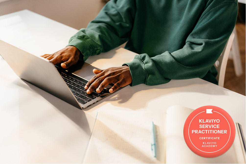 Hands typing on a laptop next to a Klaviyo Service Practitioner badge.