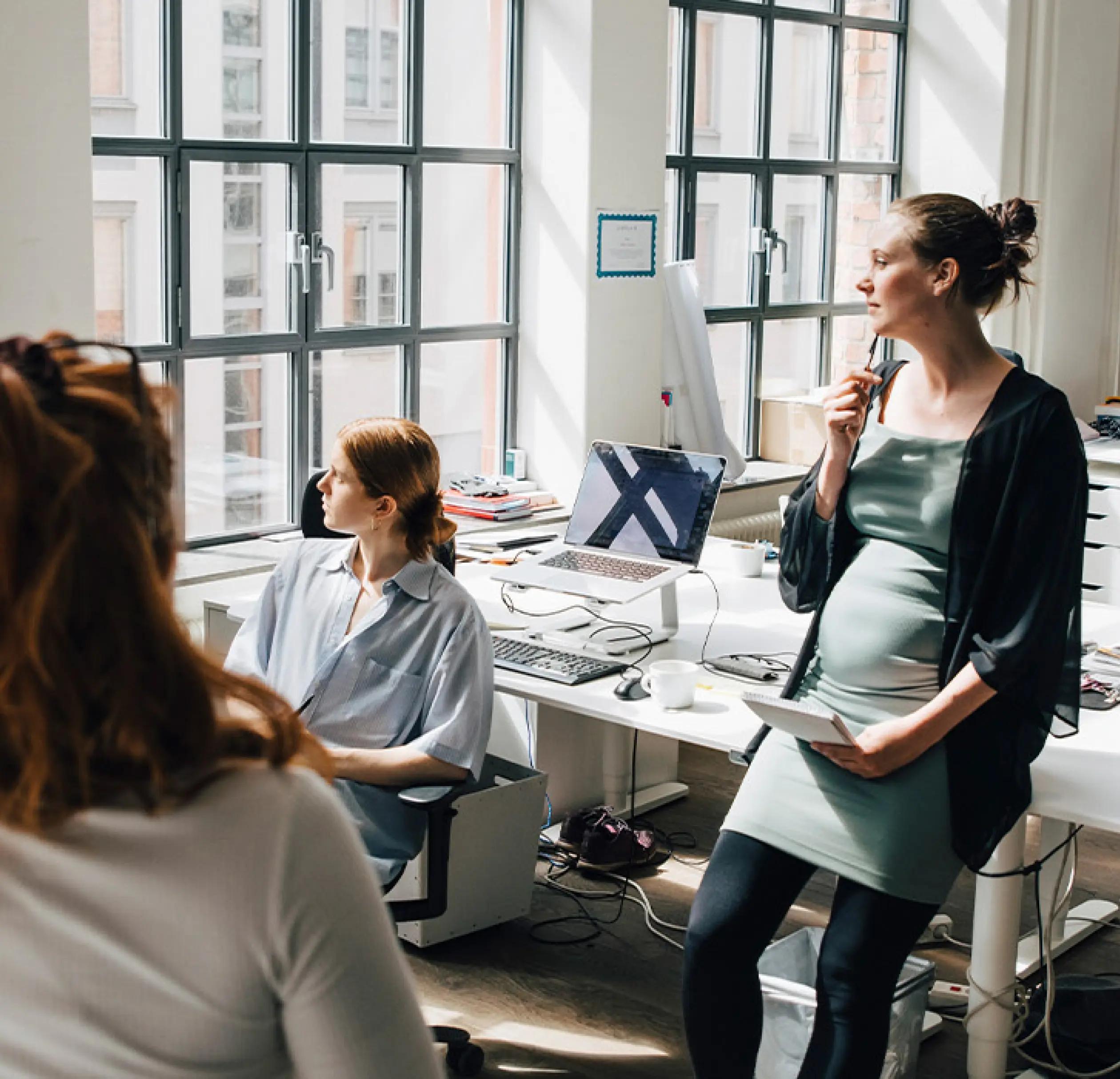 a pregnant woman sitting with her colleagues looking out the window