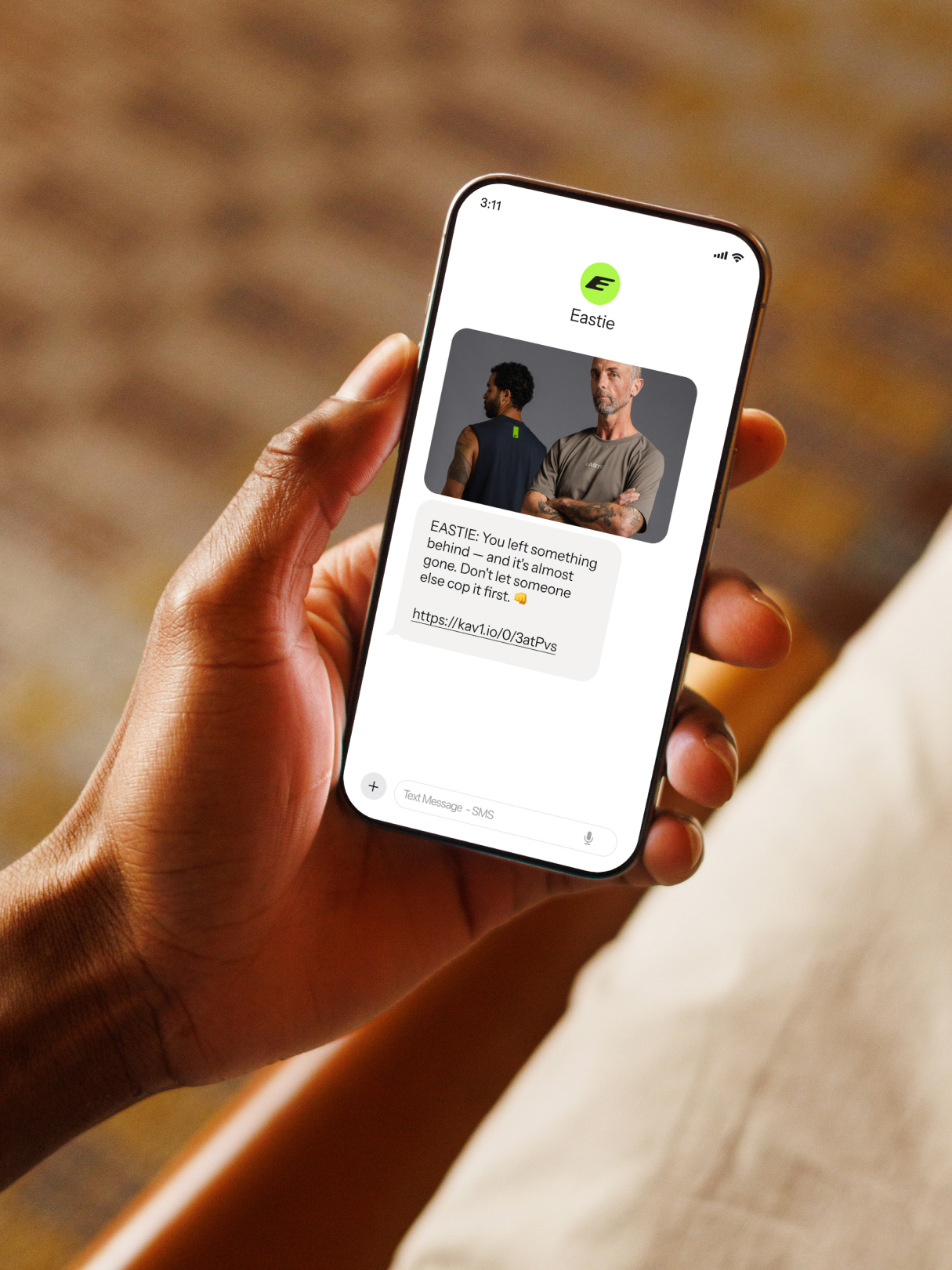 Person holding a smartphone displaying an Eastie reminder text with a clothing product photo and link.