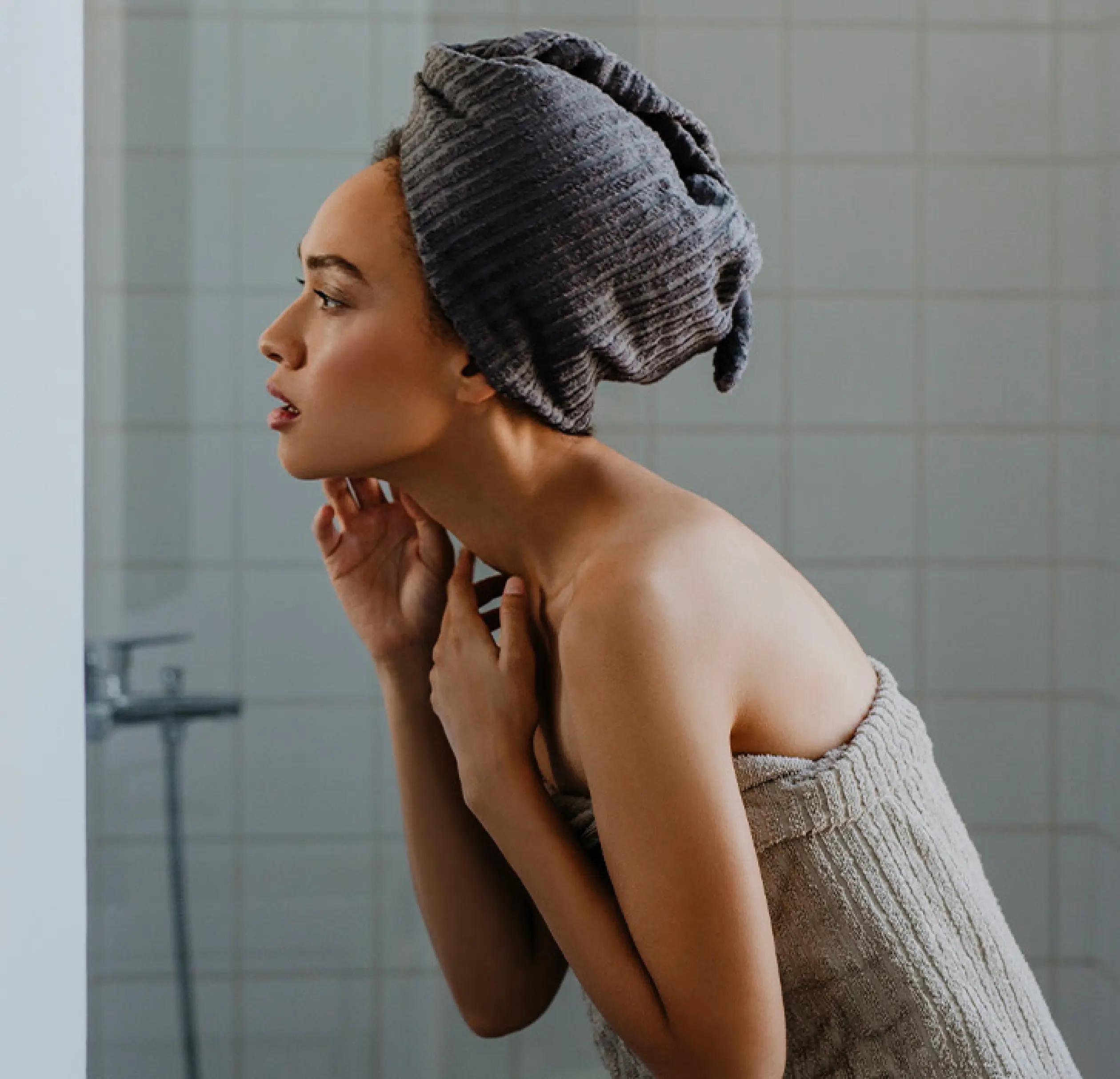 A woman in a towel turban looking at the mirror