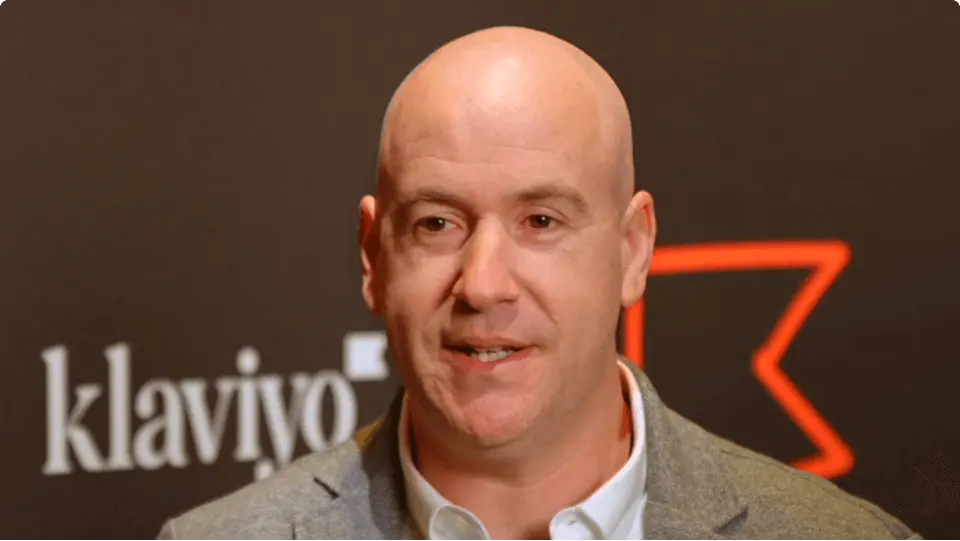 A man in a suit speaks in front of a backdrop with the Klaviyo logo.