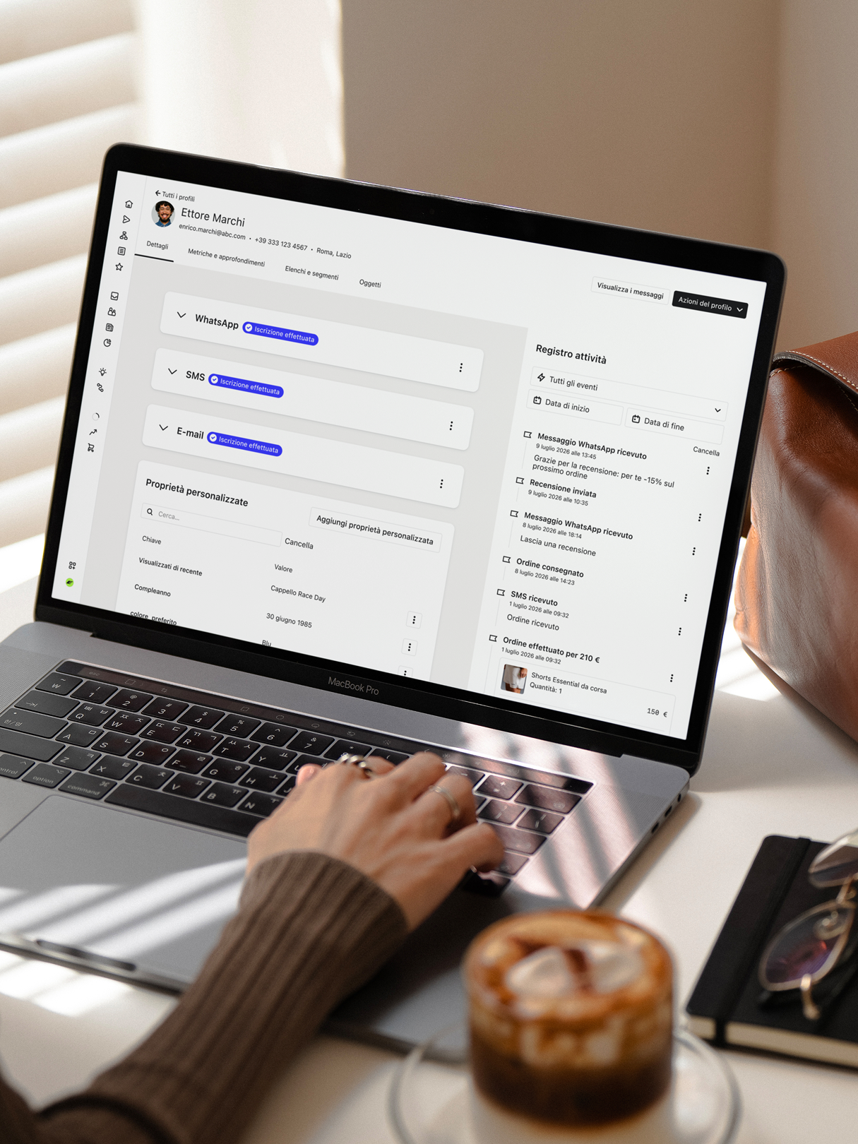 Person using a laptop displaying a customer profile and activity log beside an iced coffee.