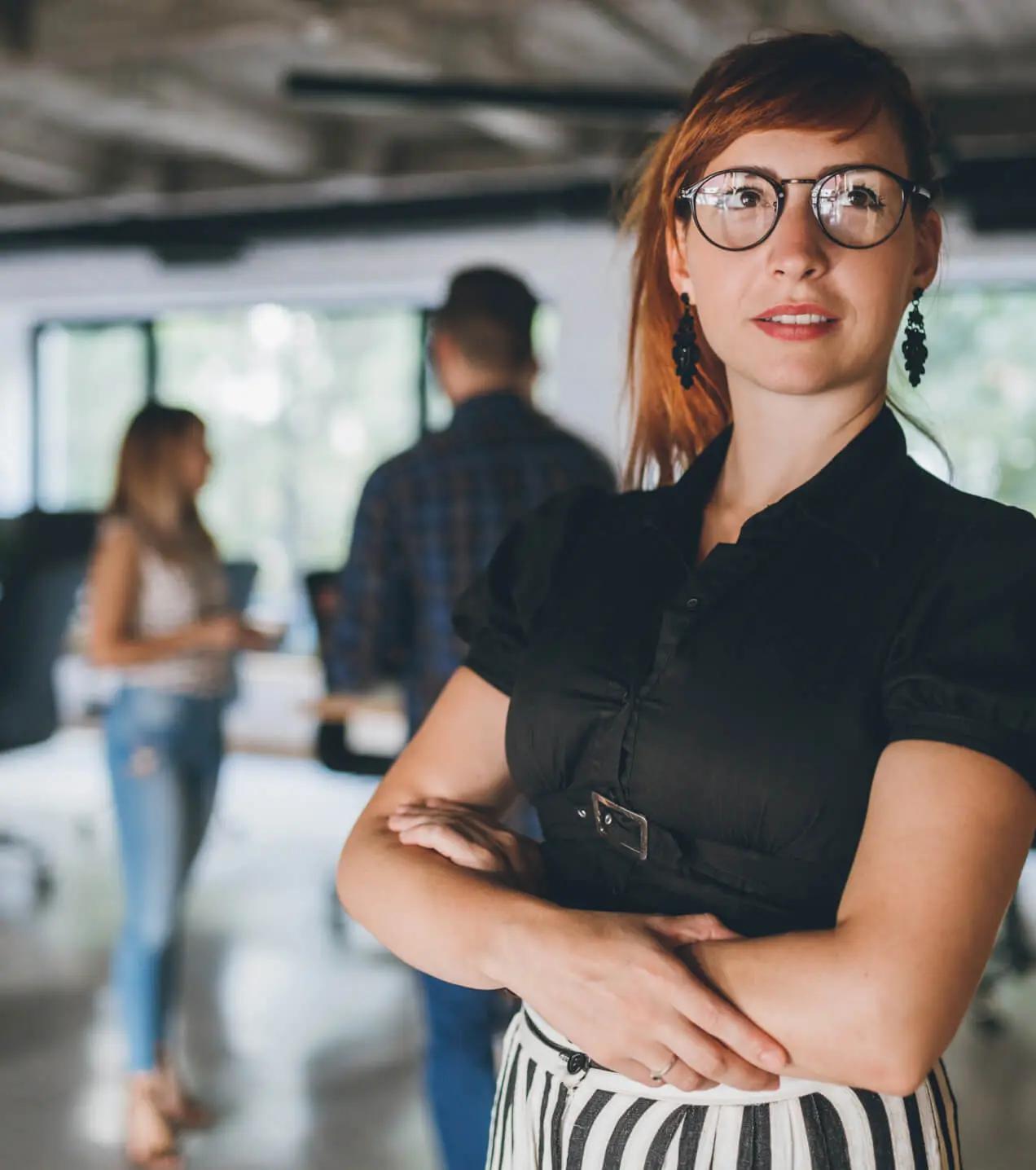 A young professional with a thoughtful look stands in a modern office, as colleagues mingle nearby.