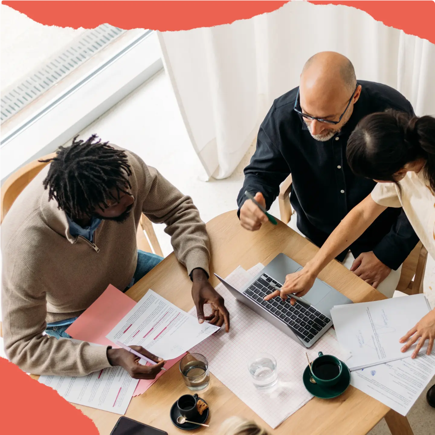 Trois personnes discutent autour d'une table avec un ordinateur portable et des documents.