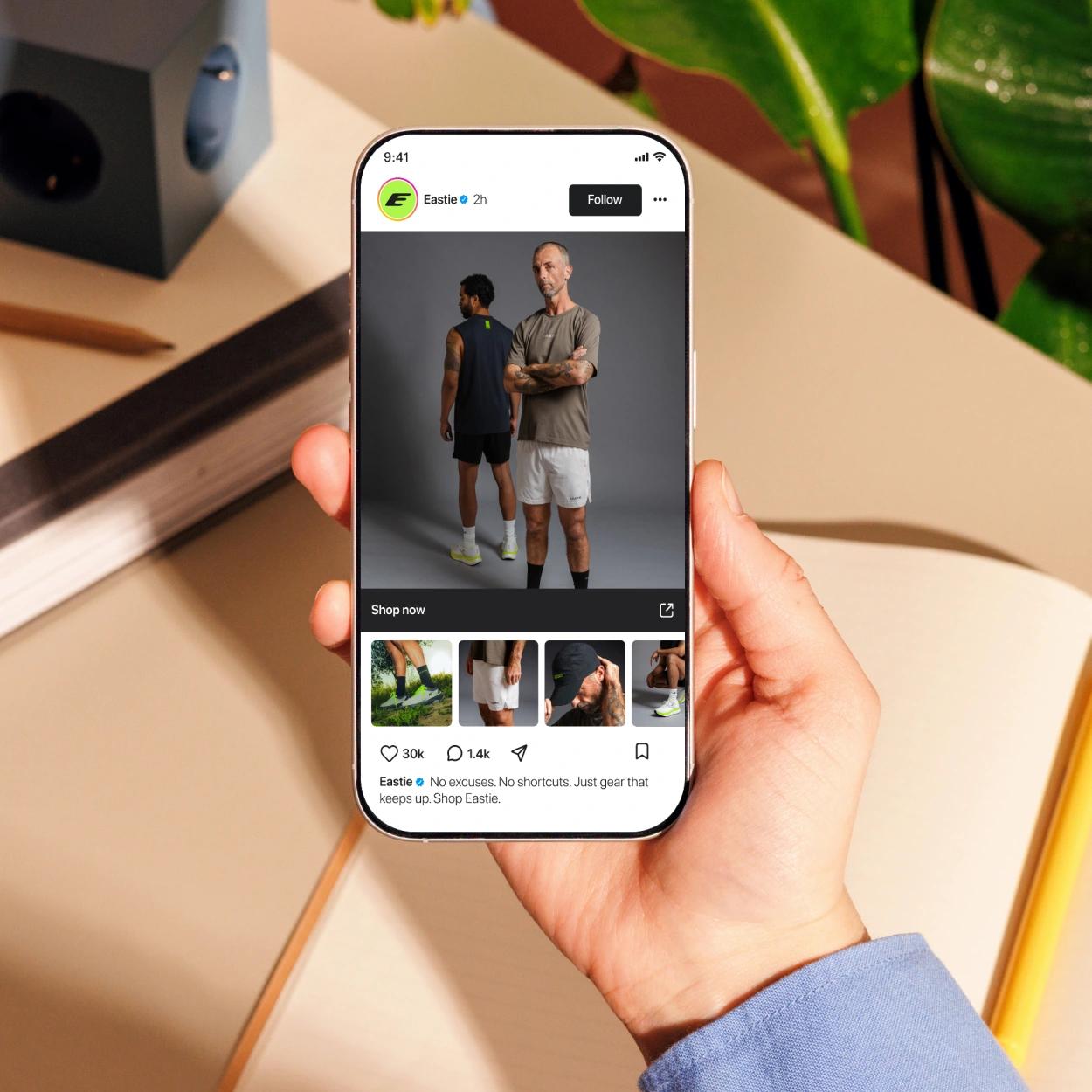 Hand holding a smartphone displaying an Eastie sportswear social media shopping post with two male models.