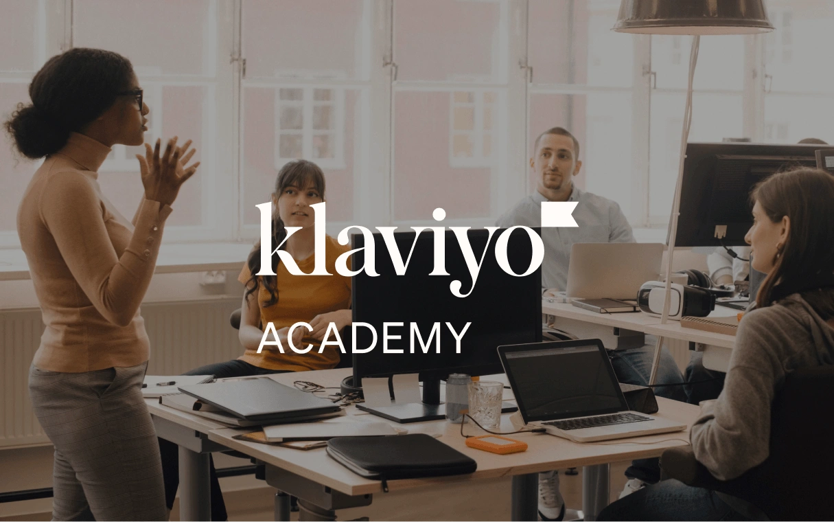 Colleagues in a bright office listen to a standing presenter, with Klaviyo Academy text overlaid.