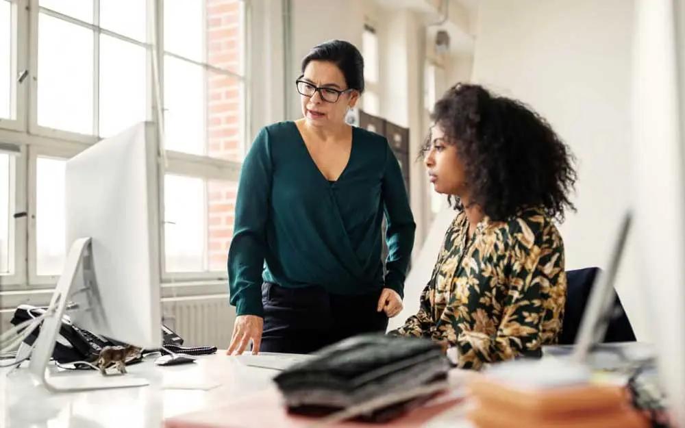 Due donne in ufficio guardano uno schermo di computer, collaborando su un progetto.