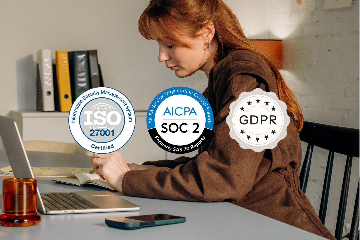 Una donna che lavora a un computer portatile con badge di conformità ISO 27001, SOC 2 e GDPR sovrapposti.