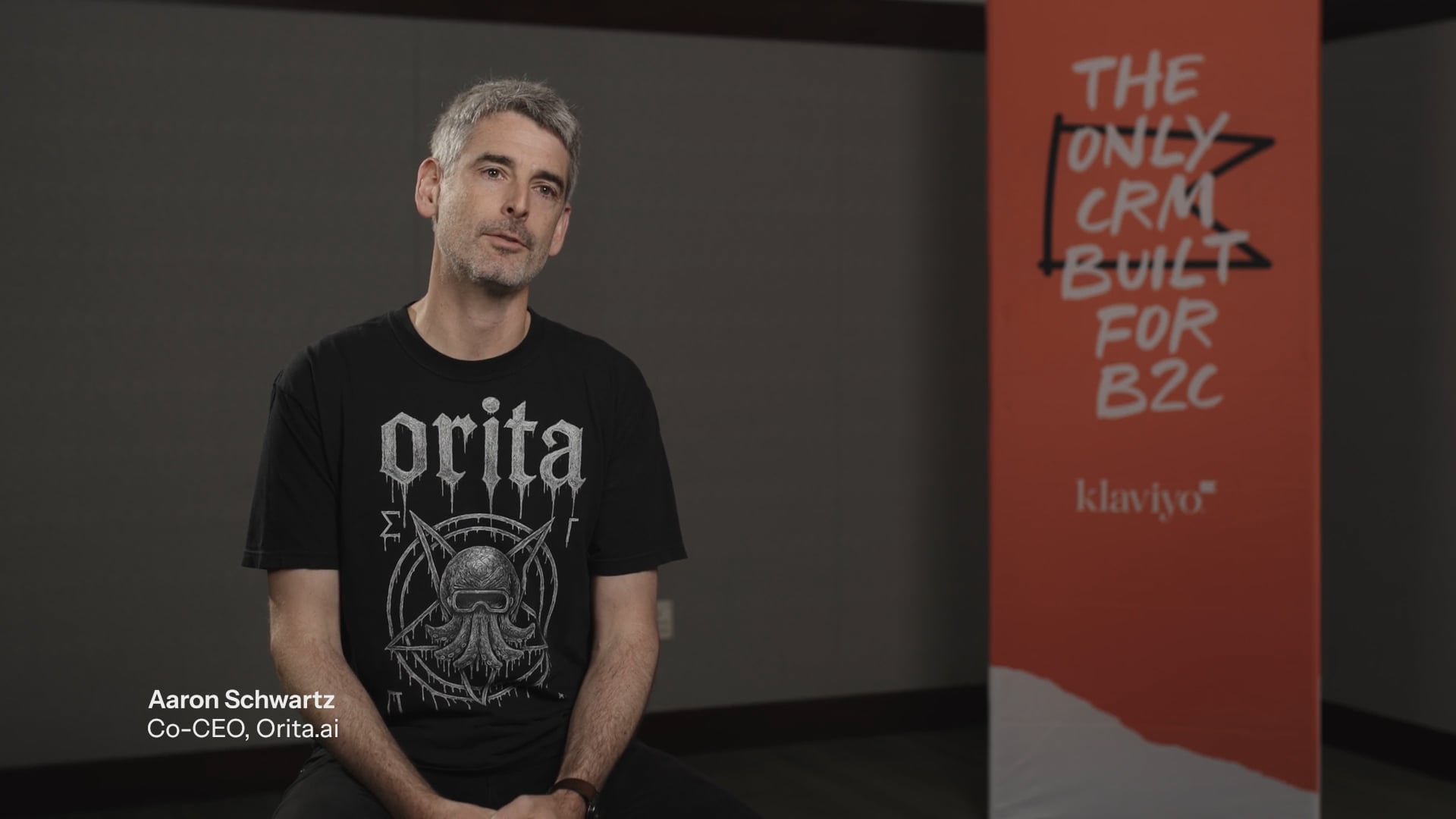 Aaron Schwartz, Co-CEO of Orita.ai, wearing an Orita t-shirt, sits next to an orange Klaviyo banner that says "The only CRM built for B2C".