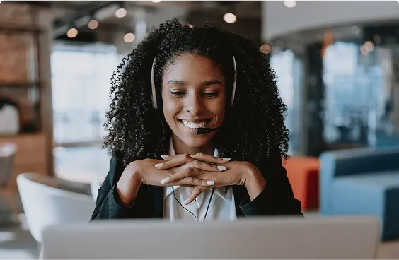 Photograph of a woman with a headset. She is looking at her laptop.