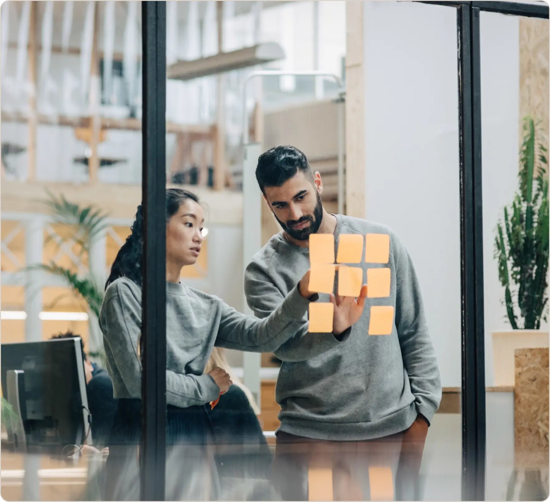 Two people discussing notes on a glass wall in an office setting.