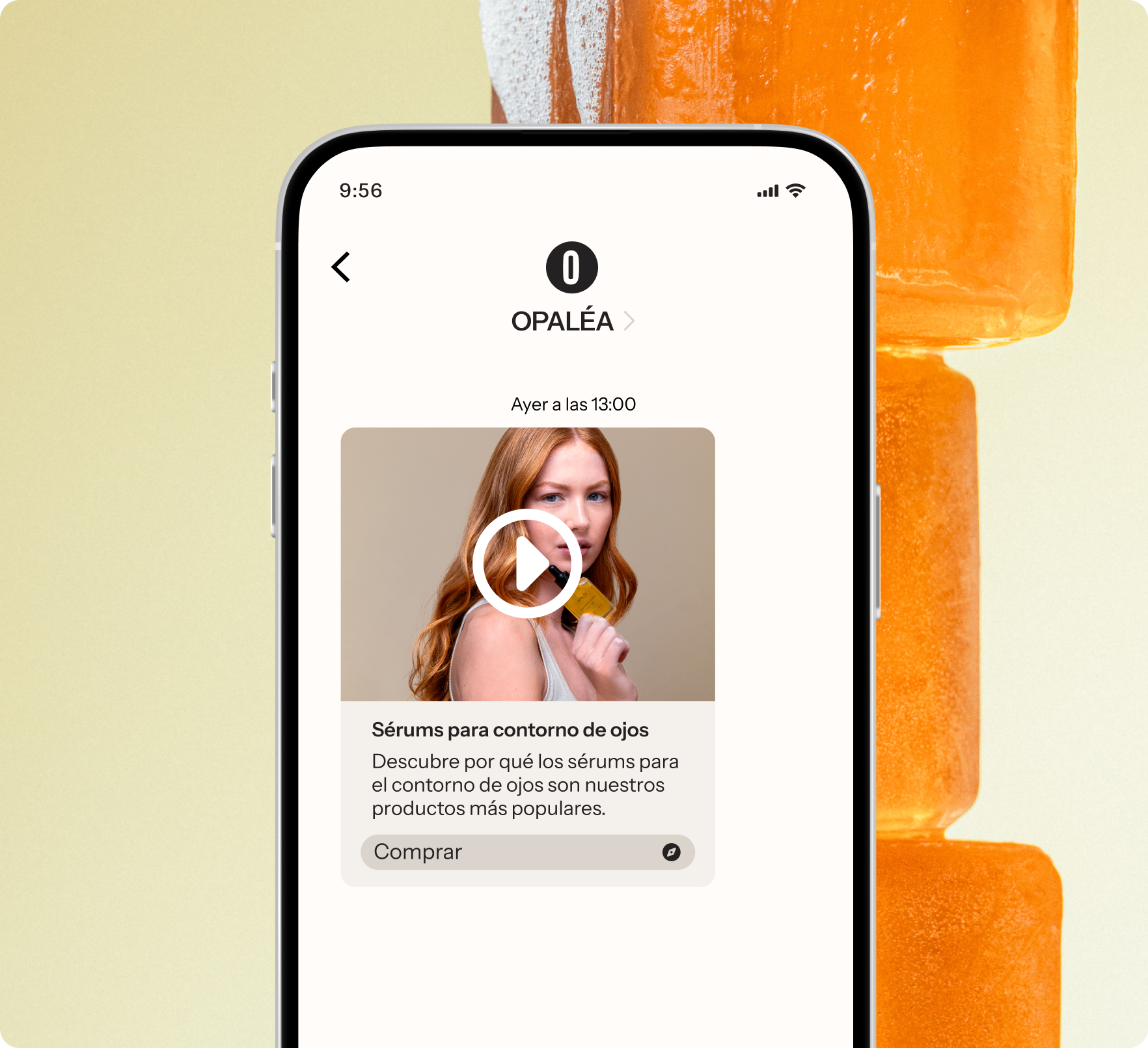 A smartphone displays an app showing a video about eye contour serums, against a background of stacked orange popsicles.