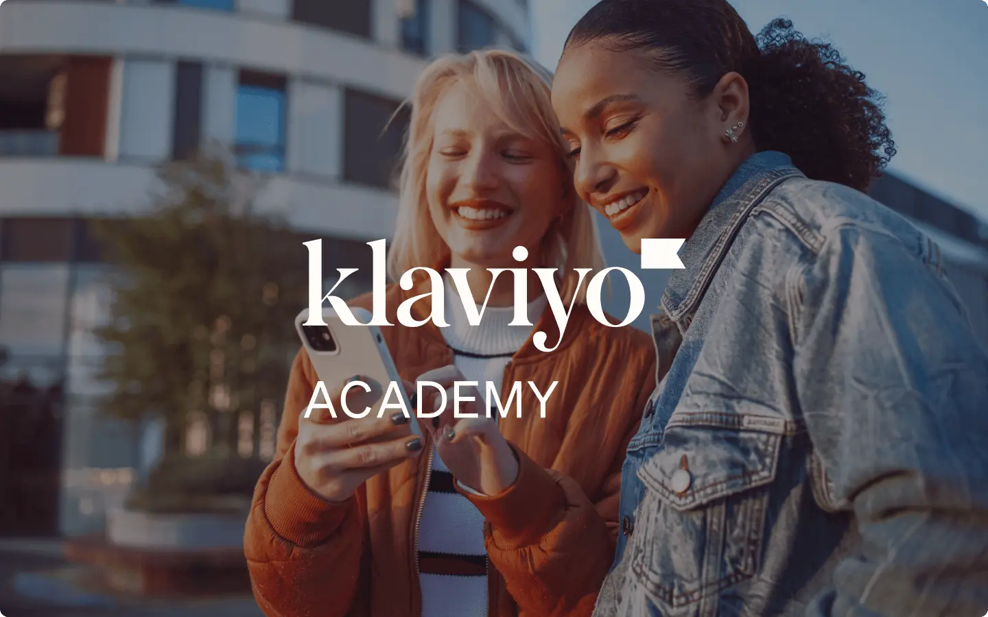 Due persone sorridenti al telefono, con il testo "Klaviyo Academy" in sovrapposizione.