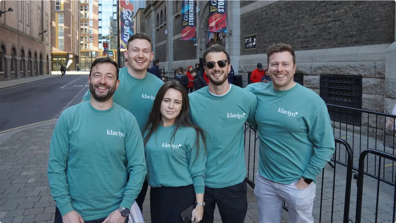 Five Klaviyos, all wearing green Klaviyo shirts, smile for a photo outside on the streets of downtown Dublin