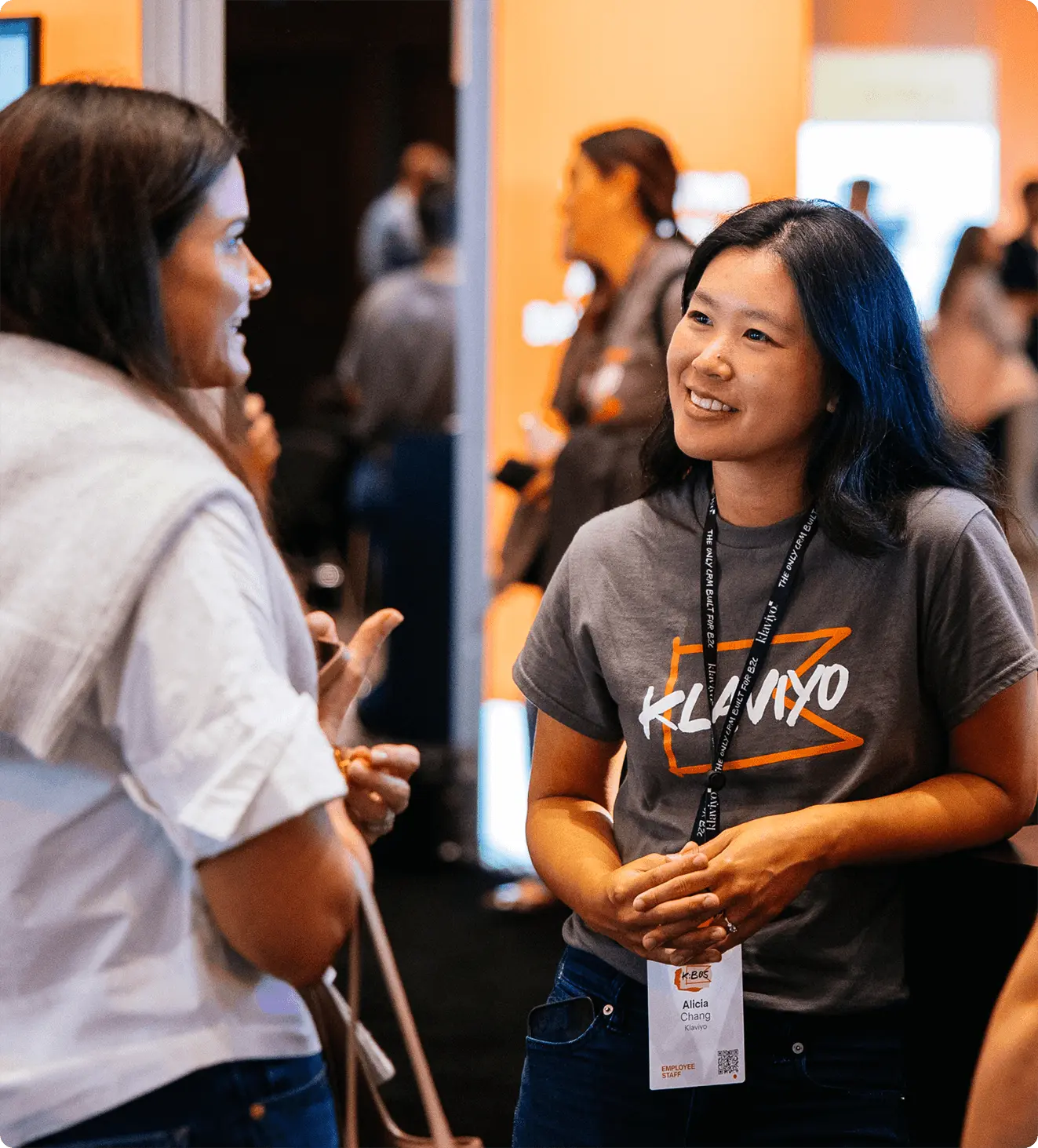 Two people talking at an event, one wearing a Klaviyo t-shirt and lanyard.