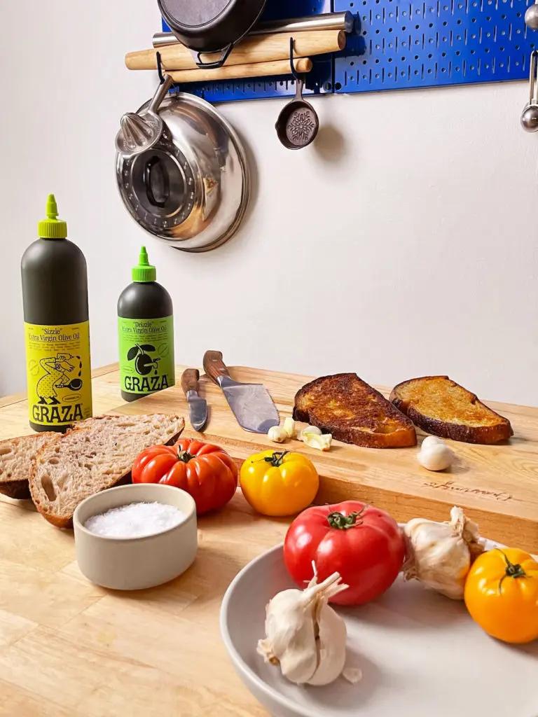 olive oil on a table with tomatoes, bread, garlic, and salt