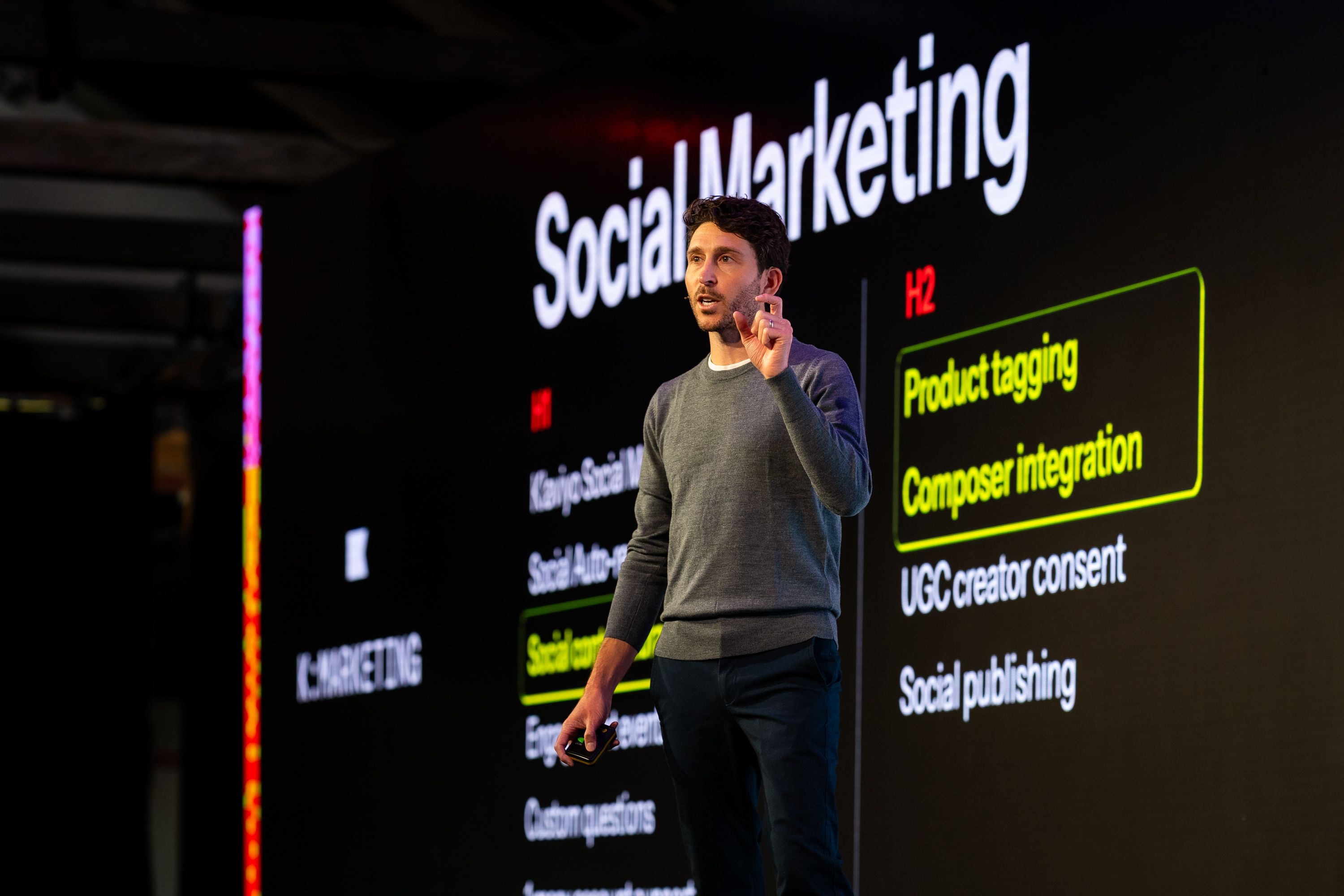 A man presents in front of a screen displaying "Social Marketing" and highlighted text "Product tagging" and "Composer integration".