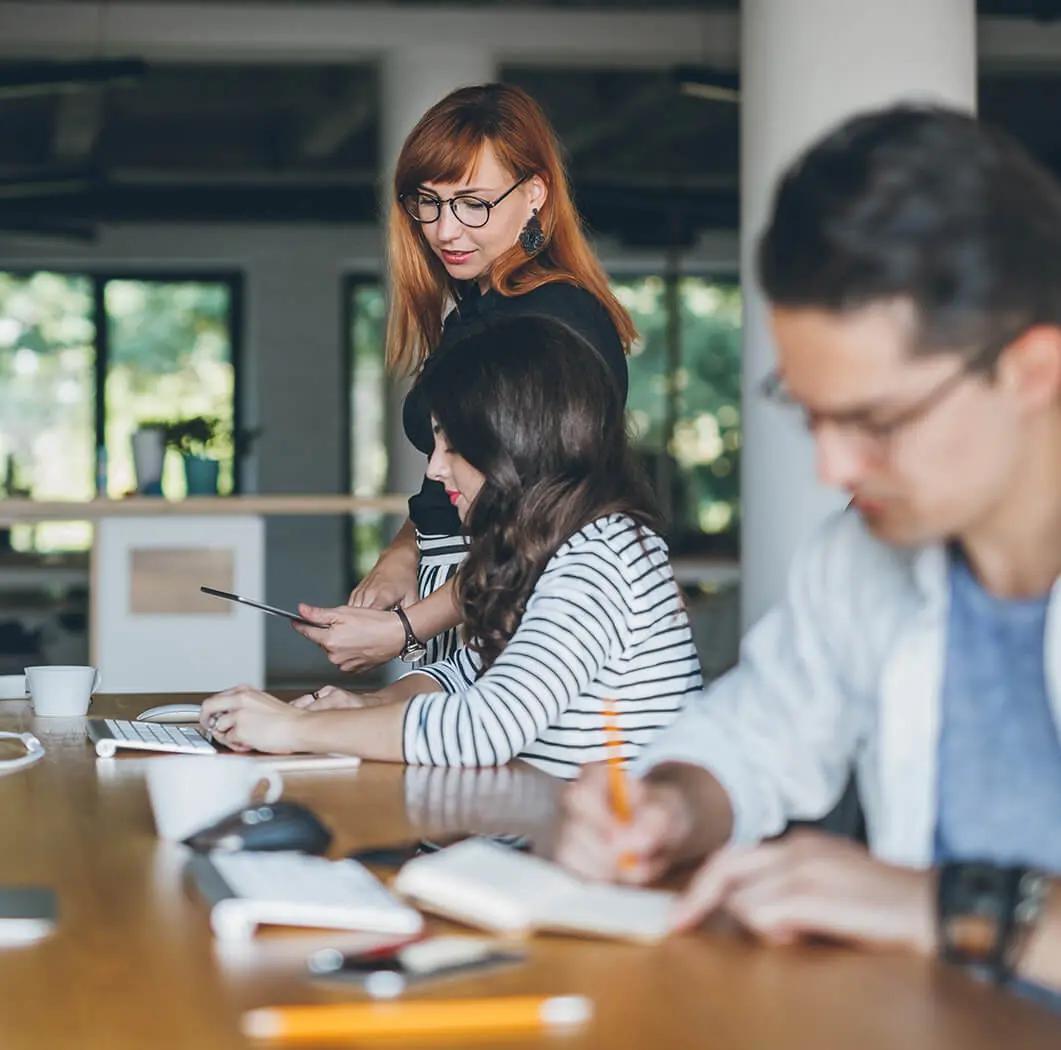 Tres personas en una oficina moderna, tomando notas, colaborando y compartiendo ideas