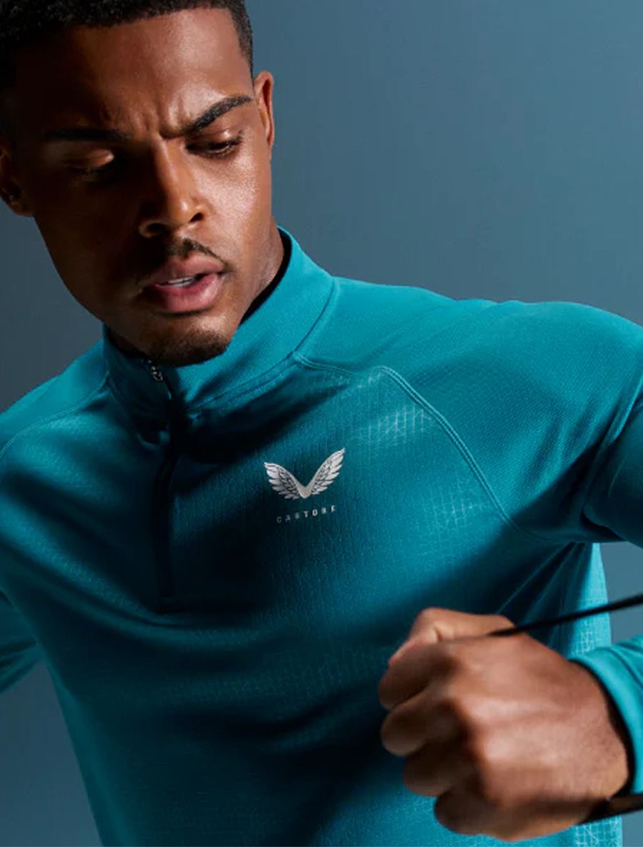 A focused man wears a teal Castore quarter-zip athletic shirt.
