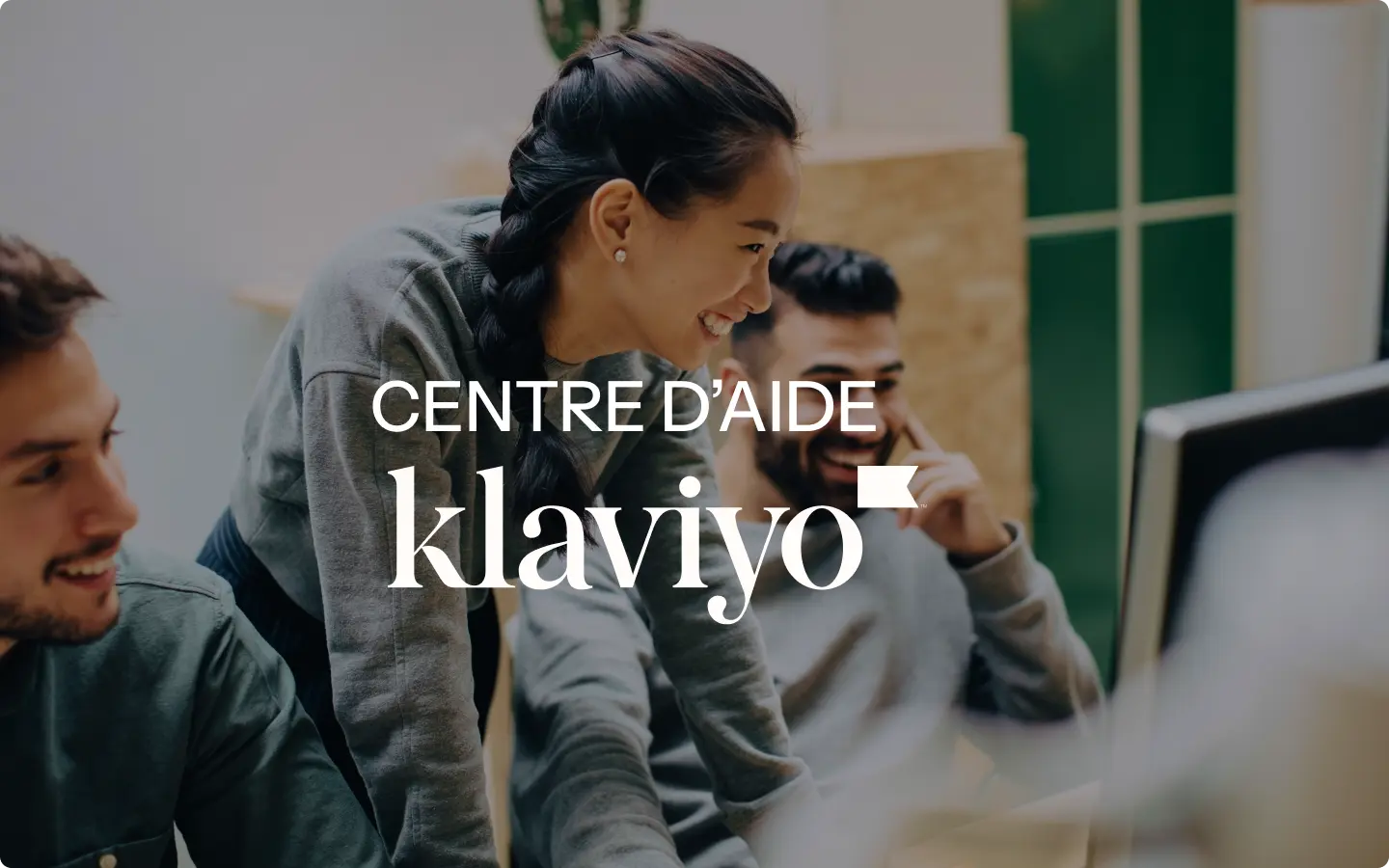 Personnes souriantes travaillant ensemble devant un ordinateur, texte "Centre d'aide Klaviyo" superposé.