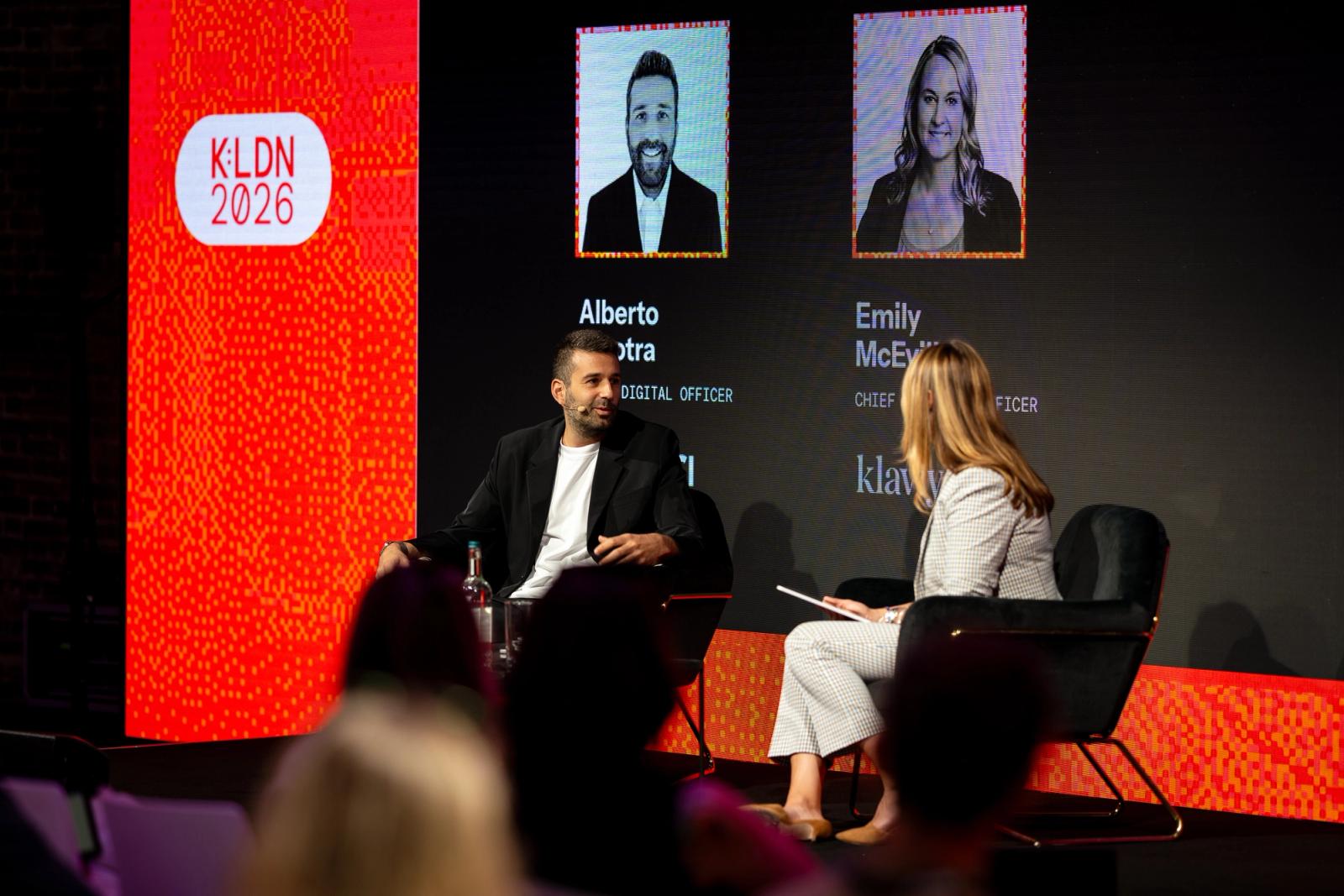 A man and a woman on stage taking part in a panel discussion, with a screen showing their names and 'K:LDN 2026'.