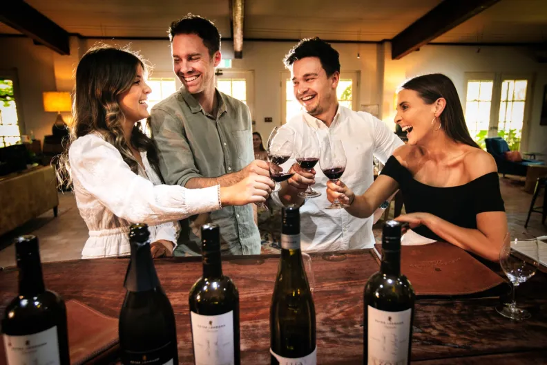 Four smiling friends toasting with red wine glasses at a tasting counter.