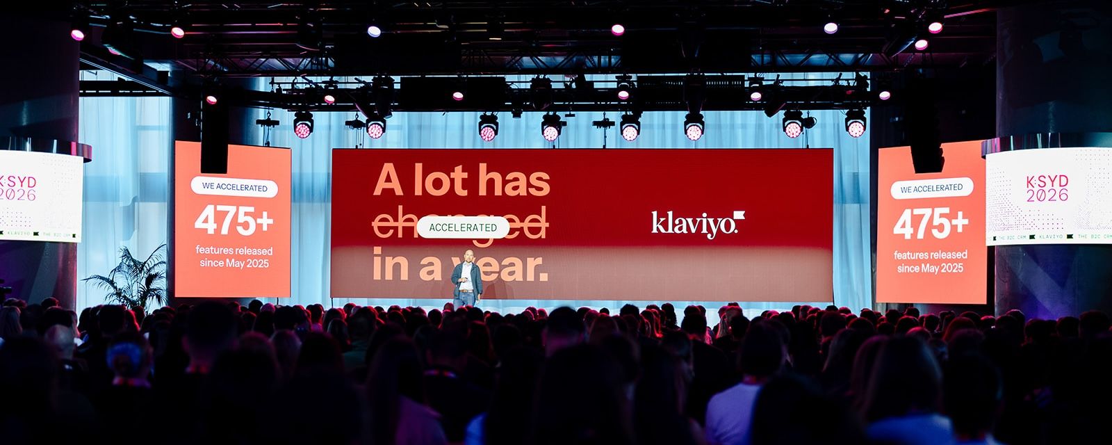 A speaker presents on stage to a large audience, with a huge screen behind displaying "A lot has changed in a year." and the Klaviyo logo, plus side screens with growth statistics.