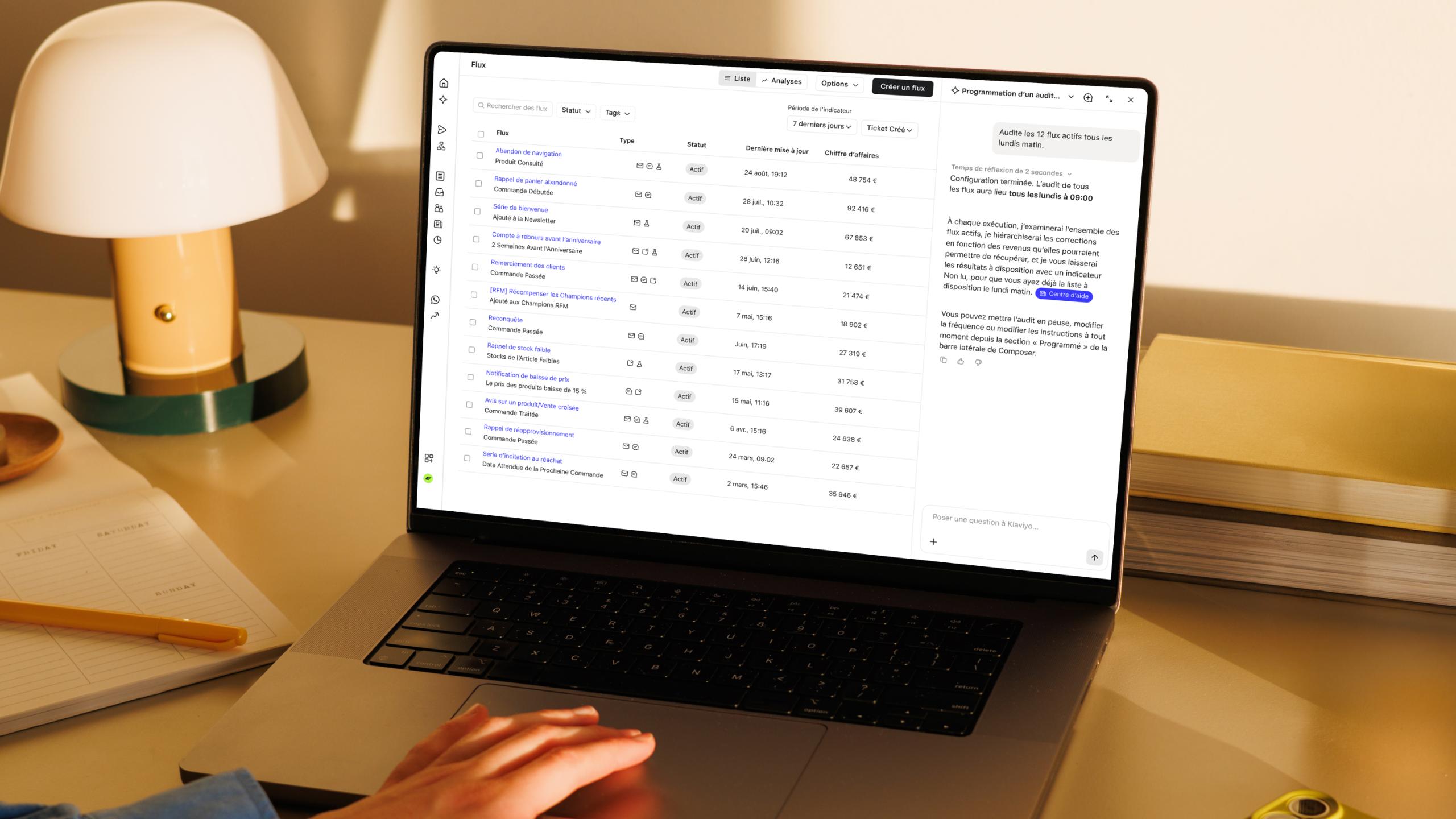 Ordinateur portable montrant un tableau de bord de marketing automation, à côté d’une lampe, d’un carnet et de livres empilés