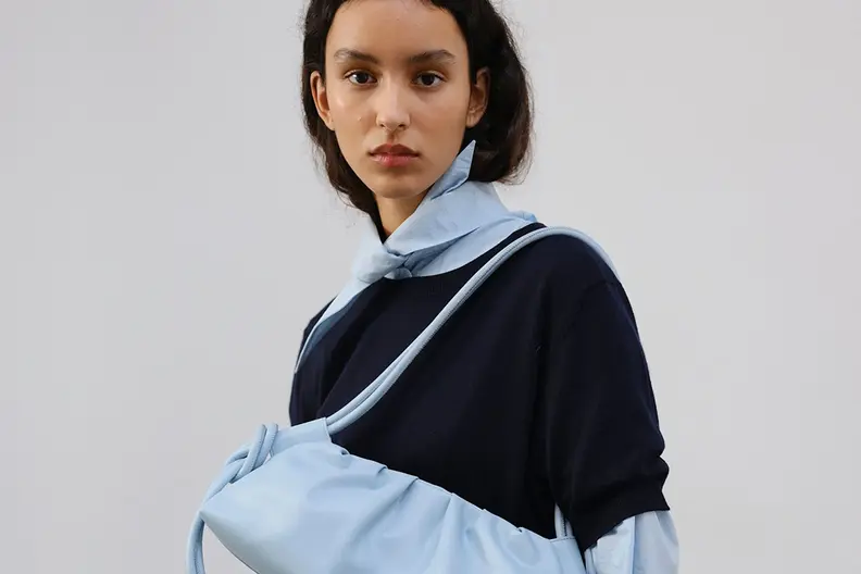 Woman in navy sweater and light blue shirt with a light blue slouchy shoulder bag.