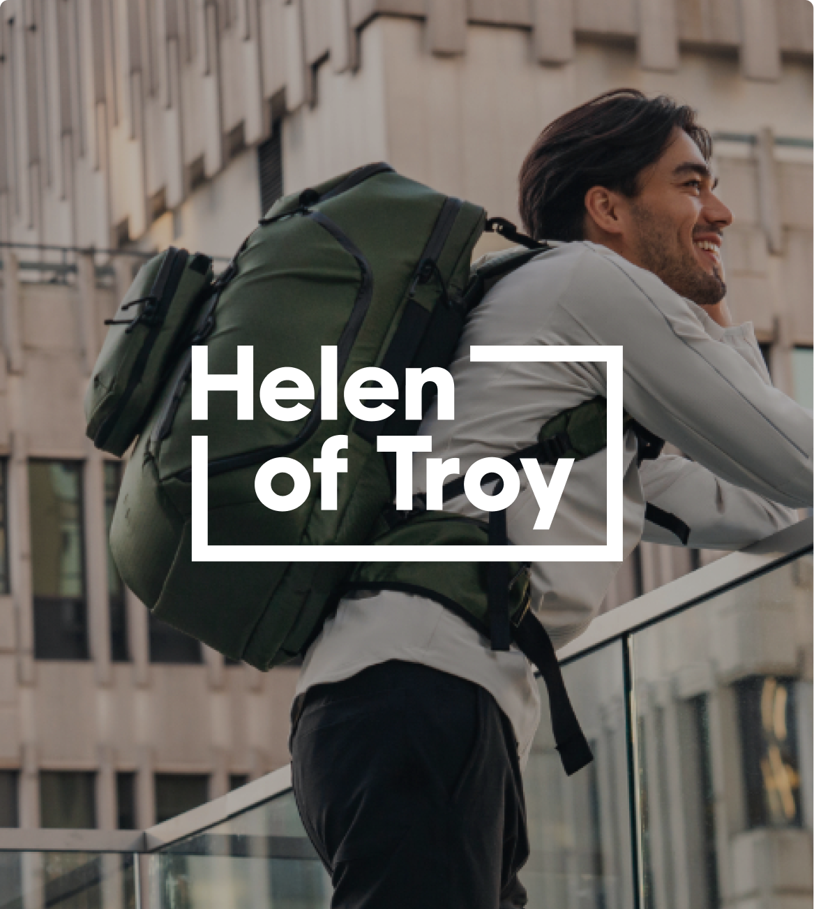 Smiling man with an olive green backpack in an urban setting, with "Helen of Troy" text.