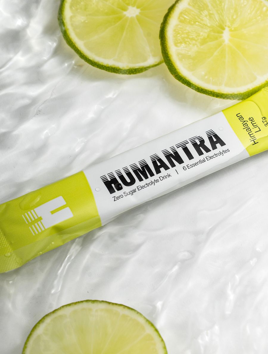 HUMANTRA Himalayan Lime electrolyte packet and lime slices on a wet white surface.