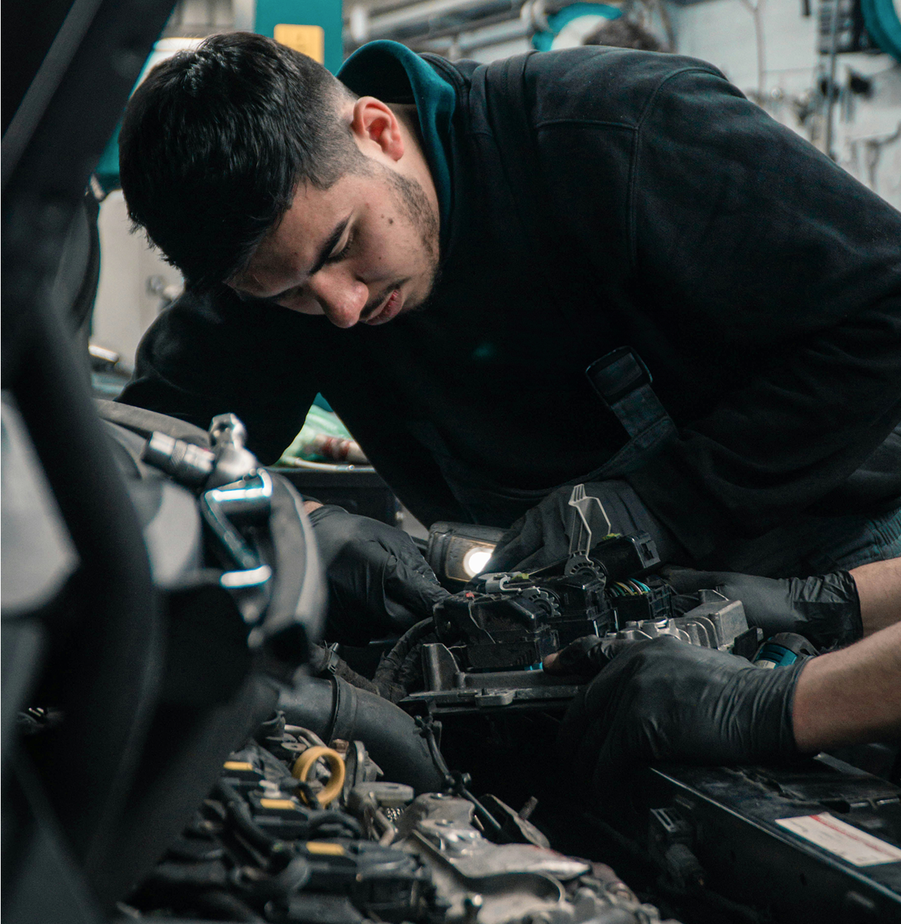 Mechanic wearing gloves works on a car engine with assistance from another pair of hands.