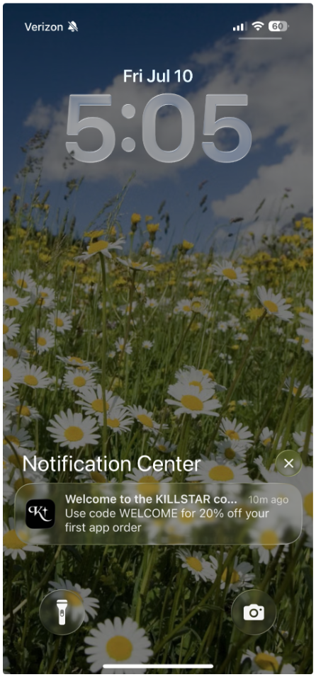 An iPhone lock screen displays the time 5:05 and date Fri Jul 10 over a background of white daisies and wildflowers, with a Killstar notification for 20% off.