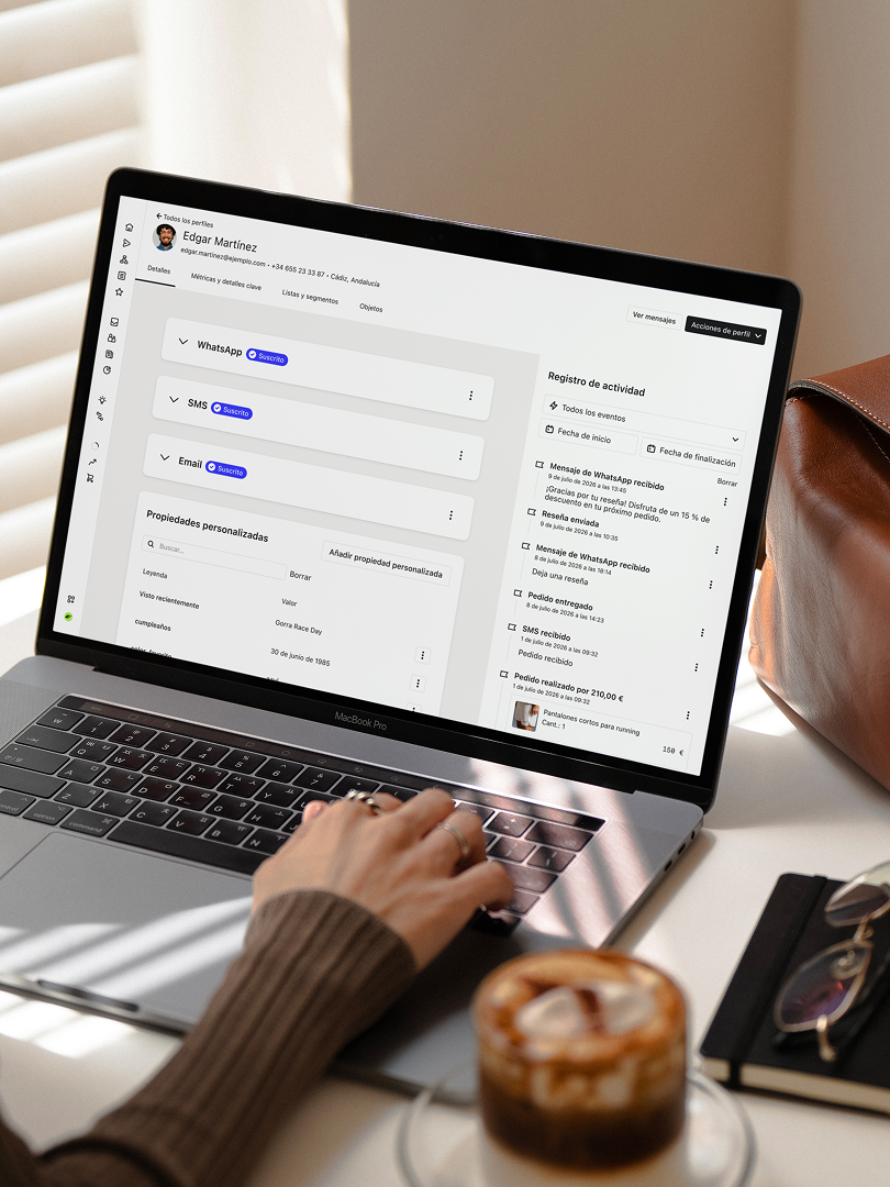 Person using a laptop displaying a customer profile and activity log beside an iced coffee.