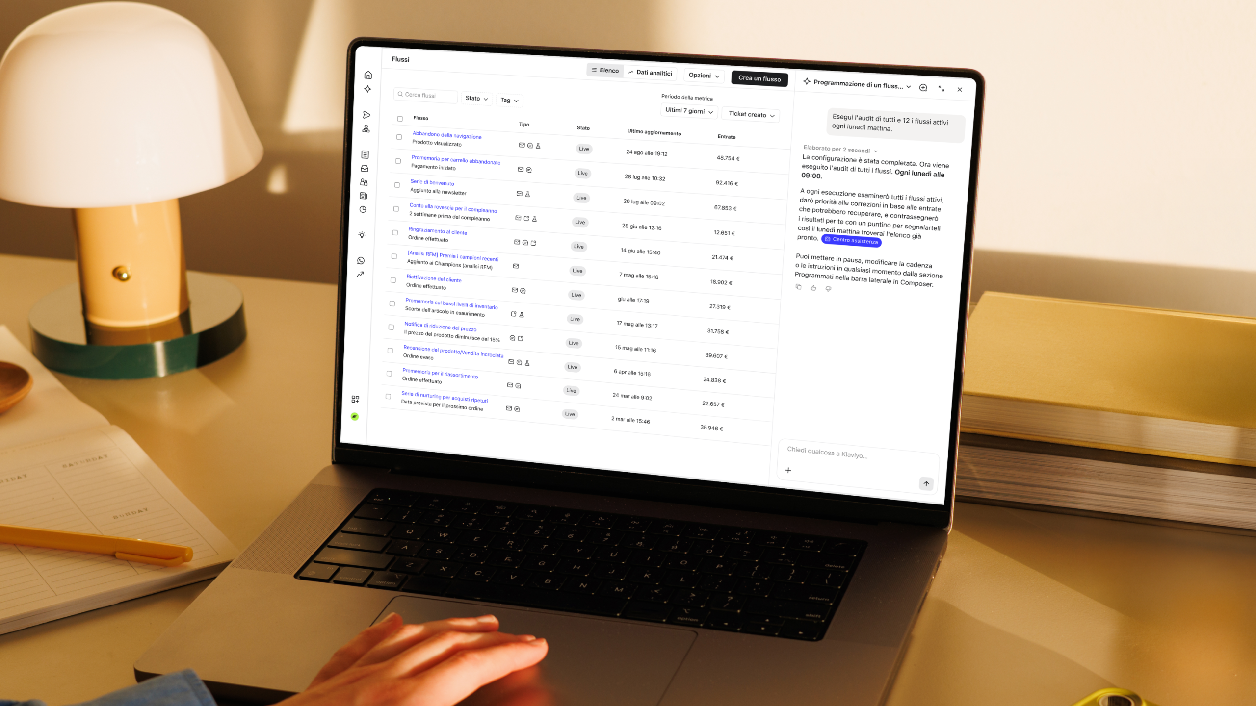 Un laptop che mostra un pannello di controllo di automazione marketing accanto a una lampada, un quaderno e una pila di libri.