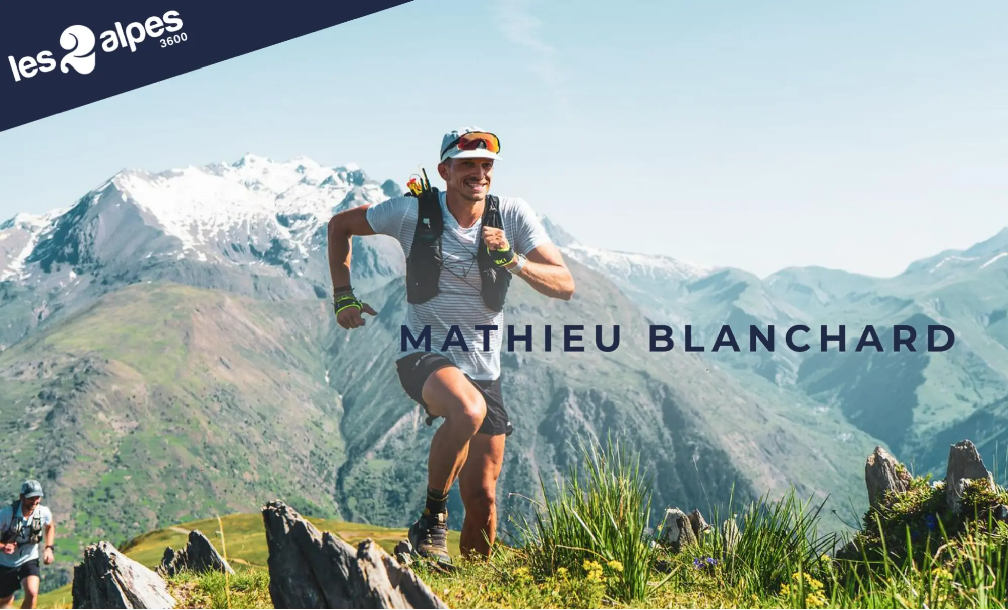 Image promotionnelle des 2 Alpes 3600 avec Mathieu Blanchard, athlète de trail running, courant en montagne avec un grand sourire. Le paysage verdoyant et les sommets enneigés illustrent la promotion d’activités estivales en station.