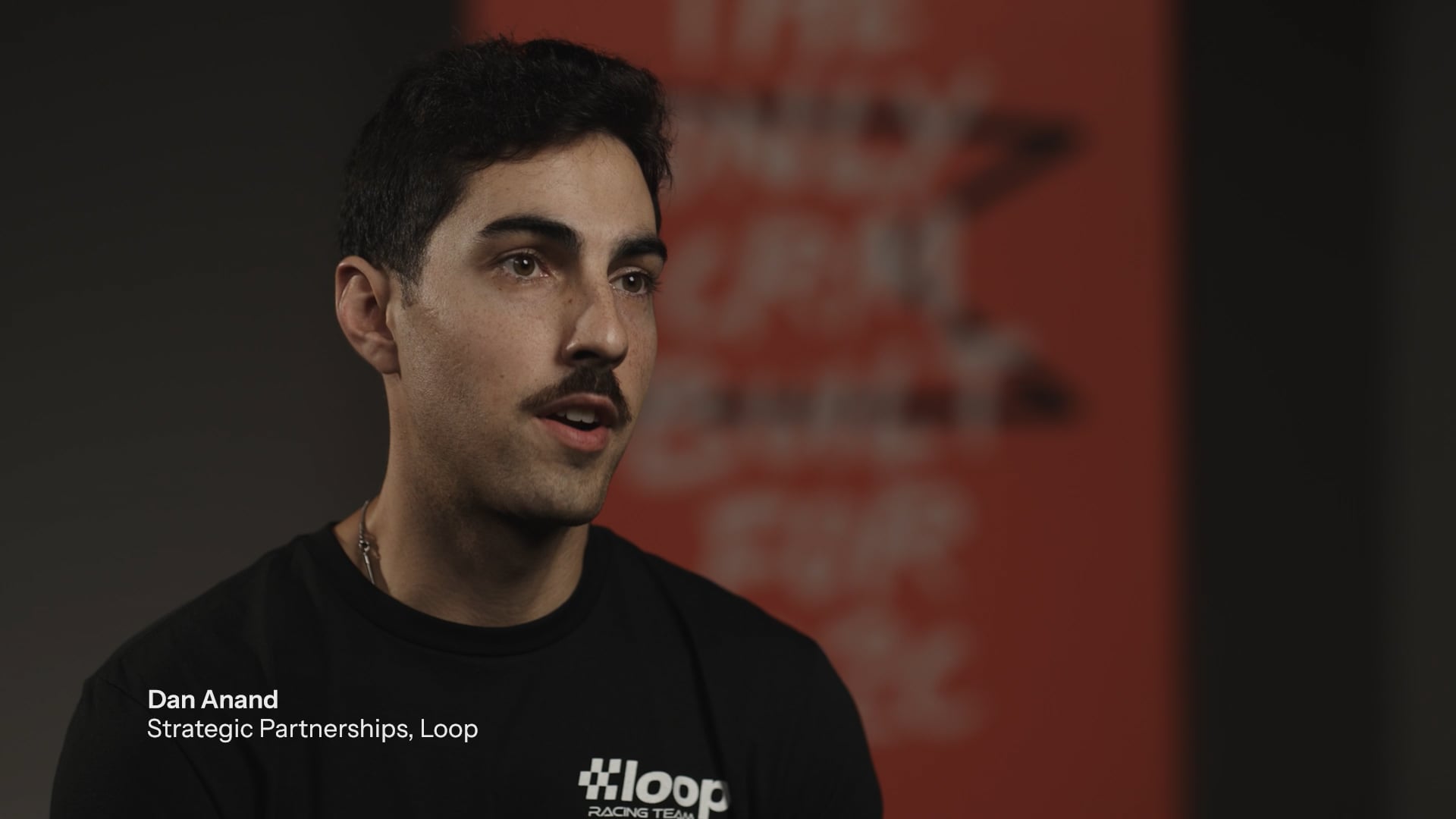 Dan Anand, Strategic Partnerships at Loop, a man with a mustache wearing a black shirt, speaking.
