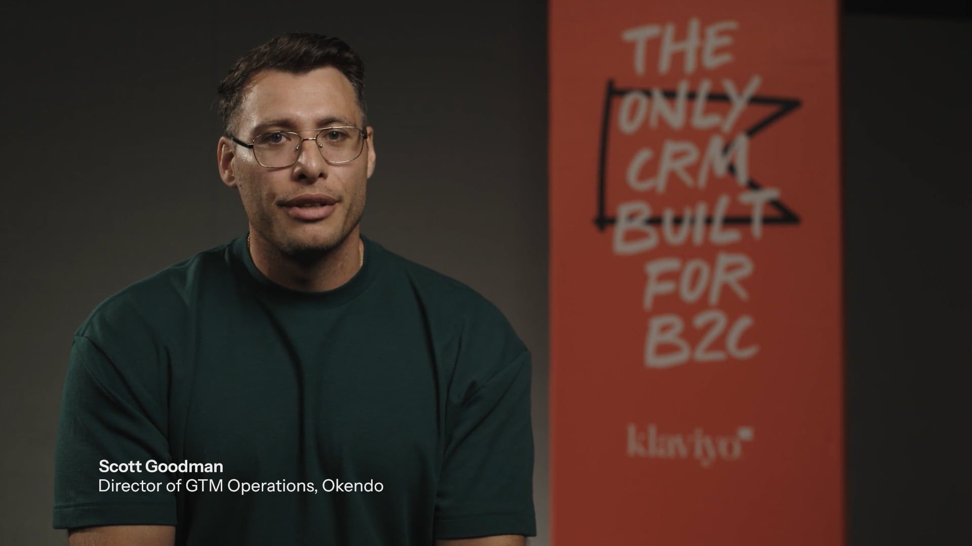 Scott Goodman, Director of GTM Operations at Okendo, speaks in front of an orange banner advertising "The Only CRM Built for B2C" by Klaviyo.