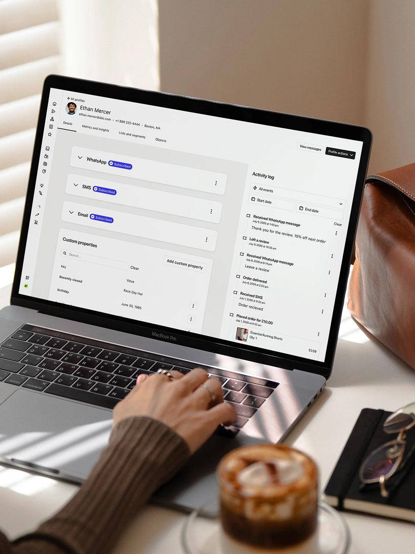 Person using a laptop displaying a customer profile and activity log beside an iced coffee.