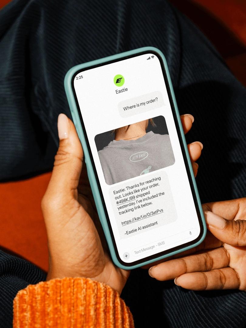 Person holds a smartphone displaying an Eastie AI text response with order tracking details.