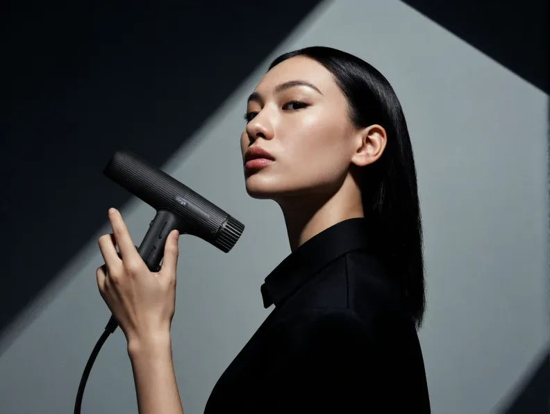 A woman with sleek dark hair holds a black, modern hair dryer.