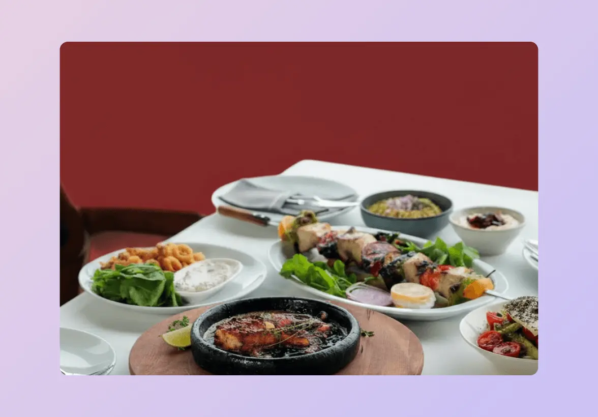 A table with various dishes, including grilled meat skewers, a sizzling platter, salads, and dips, set with plates and cutlery.