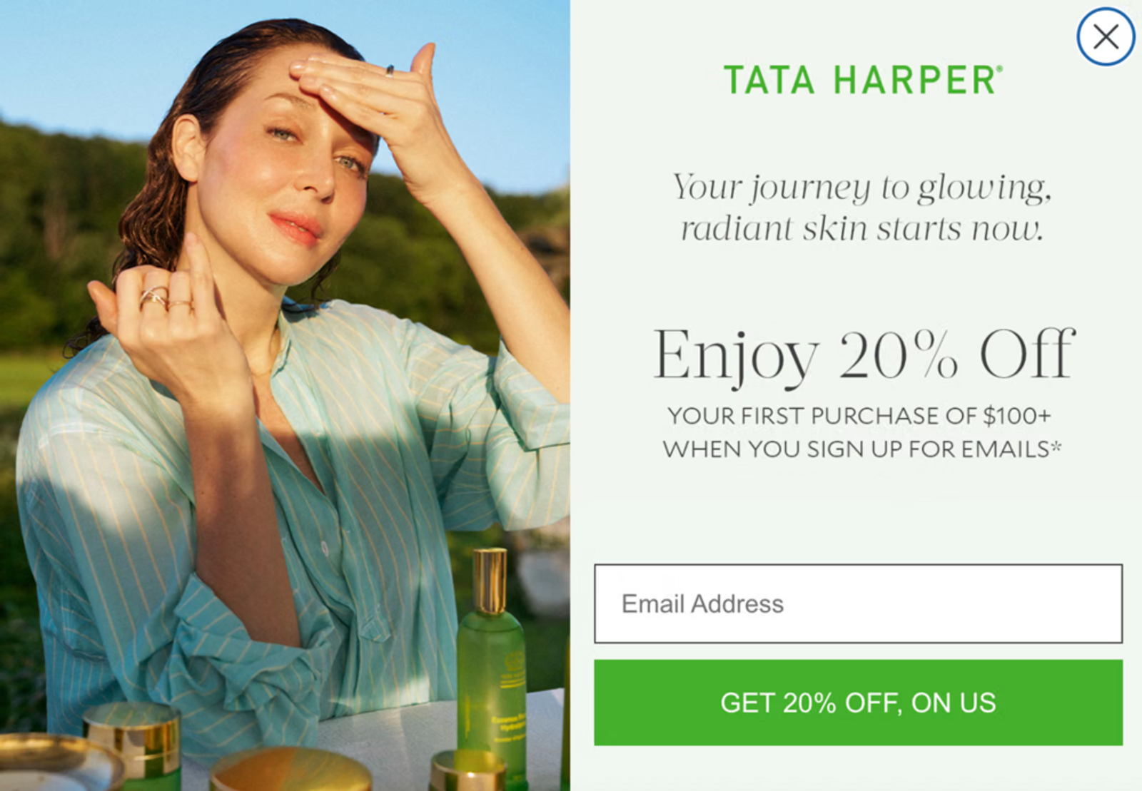 Tata Harper skincare pop-up featuring a person with light skin and wet, red hair applying skincare product to their face. They are wearing a light blue blouse with light pink stripes. The form features an offer of 20% off for email sign-up, with a green CTA button that says, “Get 20% off, on us.”