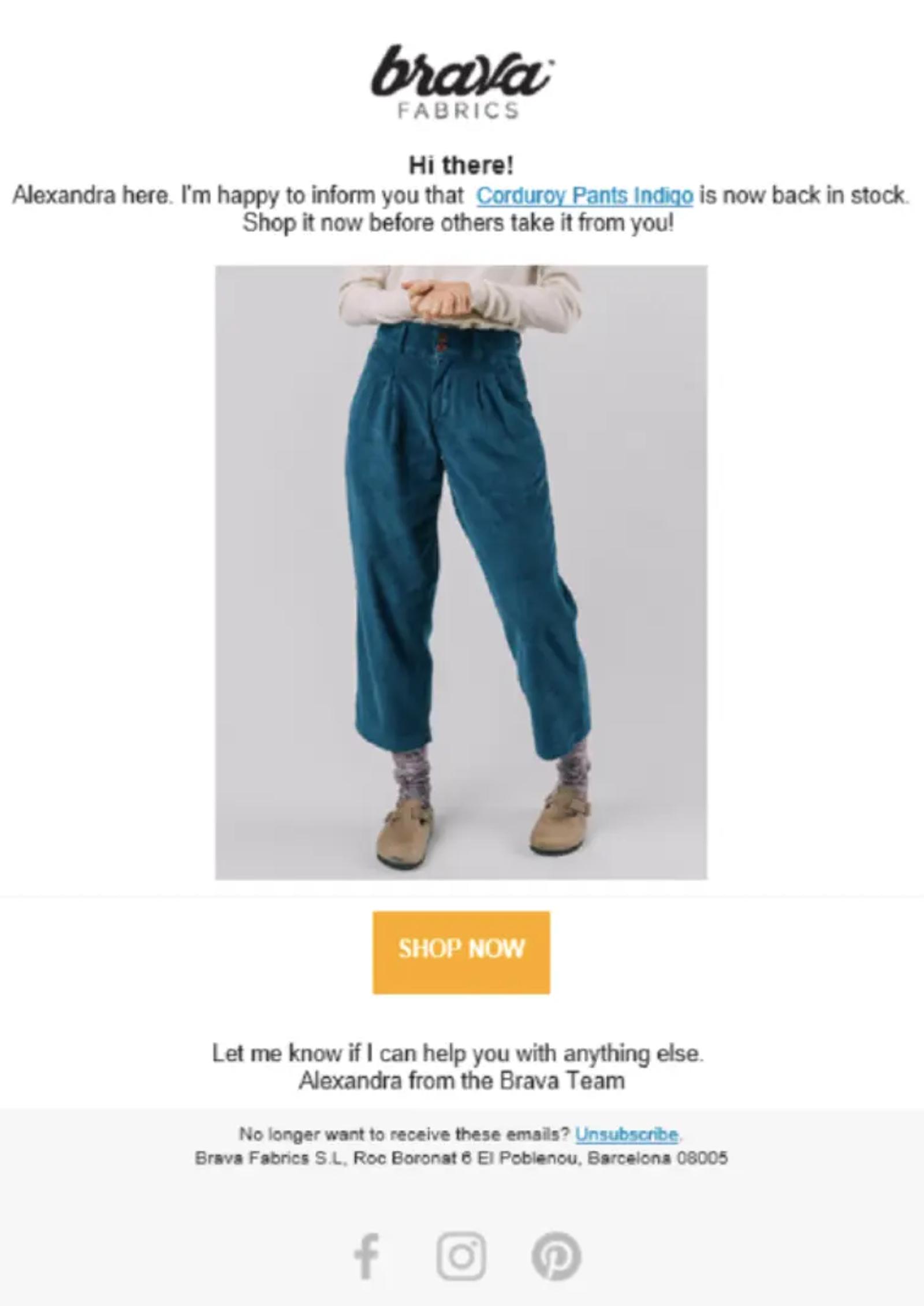 Back-in-stock email from Brava Fabrics in white, black, and teal. Under the Brava Fabrics logo and a “Hi there!” greeting, body copy reads, “Alexandra here. I’m happy to inform you that Corduroy Pants Indigo is now back in stock,” with the product name linked. A photo shows a model wearing the teal corduroy trousers. An orange “Shop now” button follows, then a sign-off: “Let me know if I can help you with anything else. Alexandra from the Brava Team.” The bottom half holds an unsubscribe link, address, and social icons.