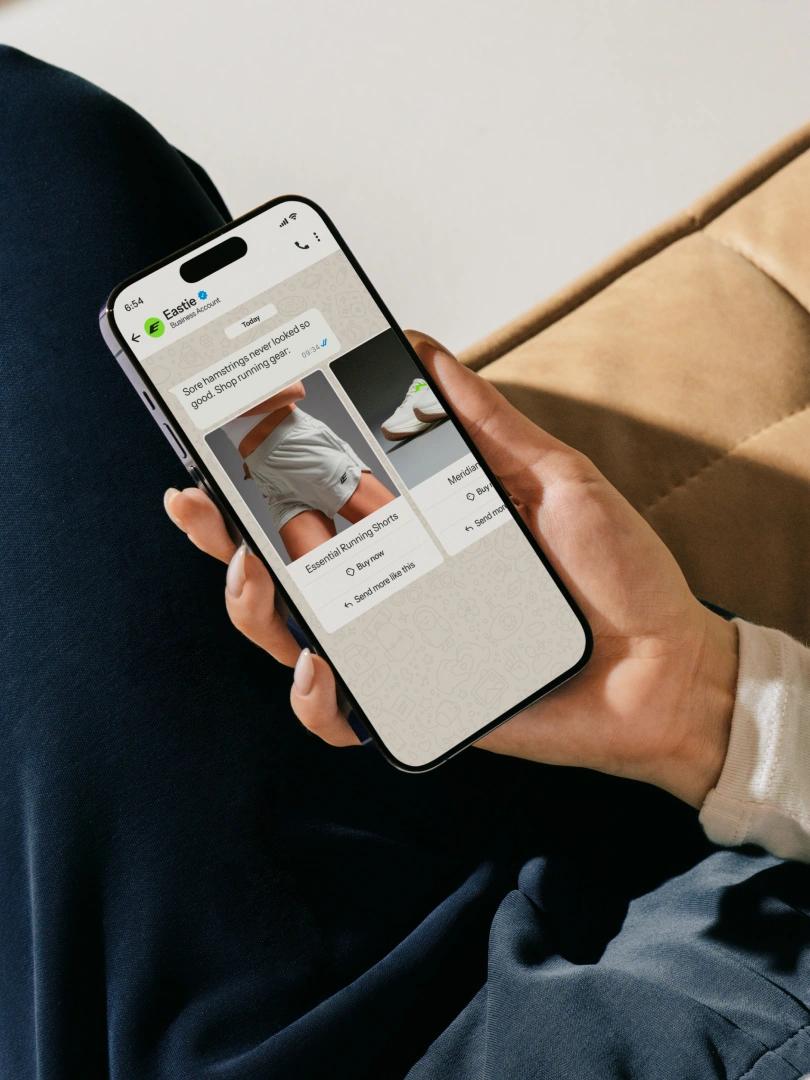 Person holding a smartphone displaying running shorts and shoes in a WhatsApp business chat