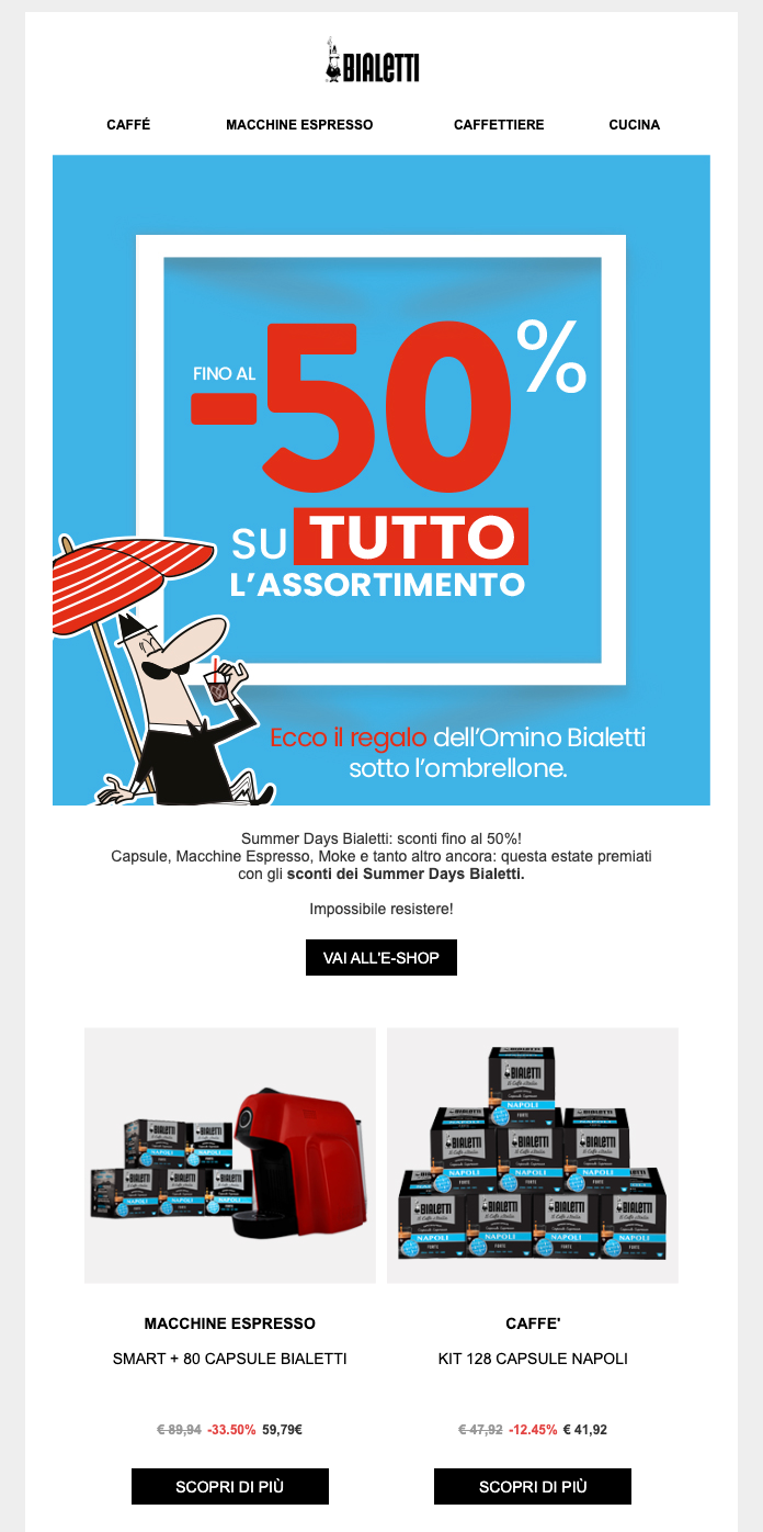 A promotional email from Bialetti for their "Summer Days" sale. At the top, the Bialetti logo is followed by a navigation menu with categories: Caffè, Macchine Espresso, Caffettiere, and Cucina.  The main banner features a bright blue background with a white square border. Inside, large red and white text reads "-50% SU TUTTO L'ASSORTIMENTO" (Up to 50% off the entire assortment). To the left, a cartoon of the iconic "Omino Bialetti" (little man with a mustache) is seen relaxing under a red and white striped beach umbrella, wearing sunglasses and holding a drink. Below the banner, the text reads: "Ecco il regalo dell’Omino Bialetti sotto l’ombrellone."  The body of the email includes a brief description of the sale and a black "VAI ALL'E-SHOP" button. Below this, two product deals are showcased:  Left: A red "Smart" espresso machine with 80 capsules, priced at 59,79€ (reduced from 89,94€, a 33.50% discount).  Right: A kit of 128 "Napoli" coffee capsules, priced at 41,92€ (reduced from 47,92€, a 12.45% discount).  Each product has a black "SCOPRI DI PIÙ" (Find out more) button underneath.