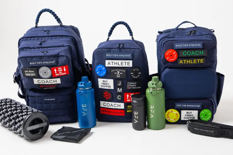 Three navy blue "Built For Athletes" gym bags with custom patches, along with water bottles and a foam roller.