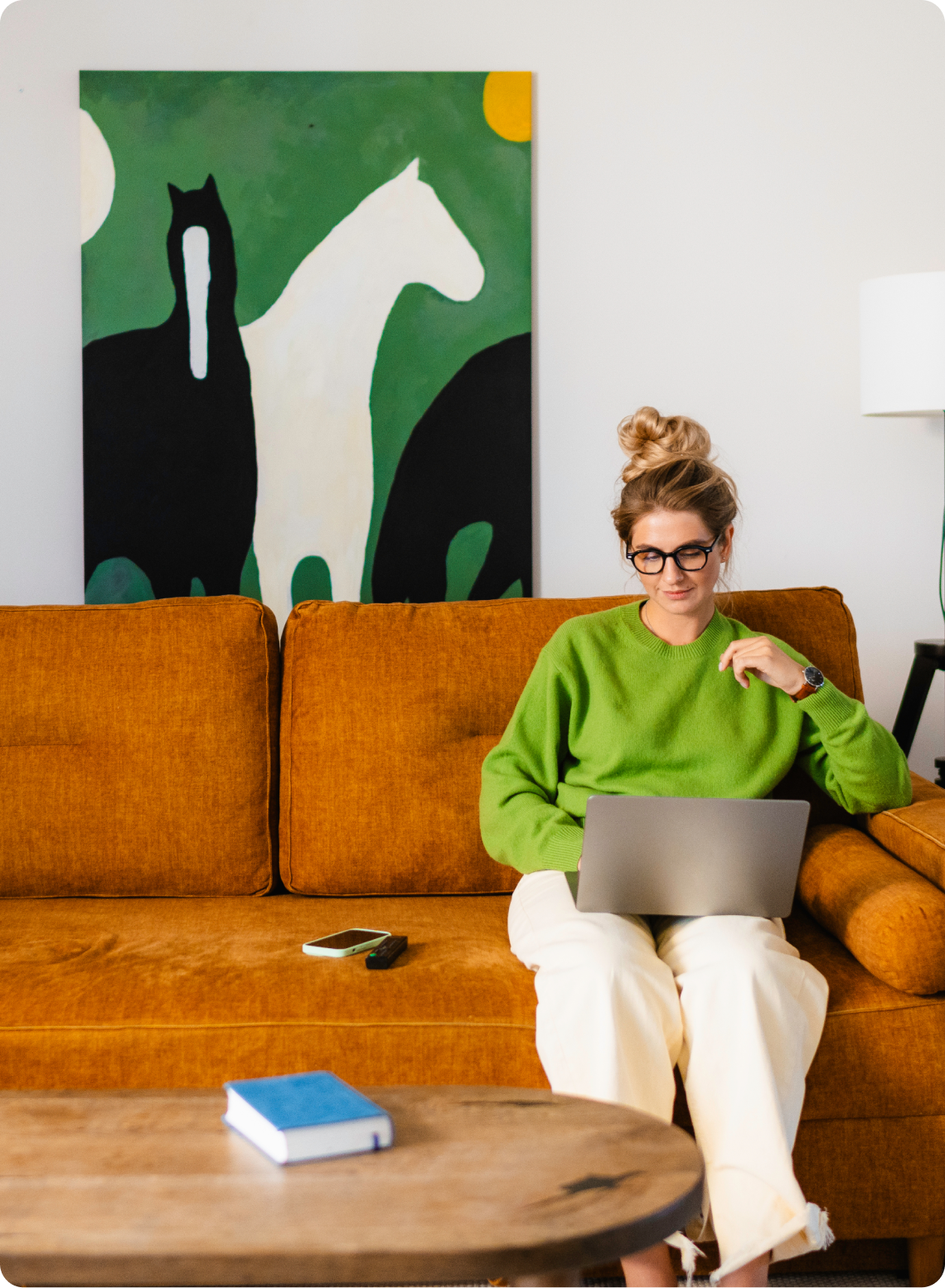 A photograph of a woman sitting on a sofa and using a laptop.