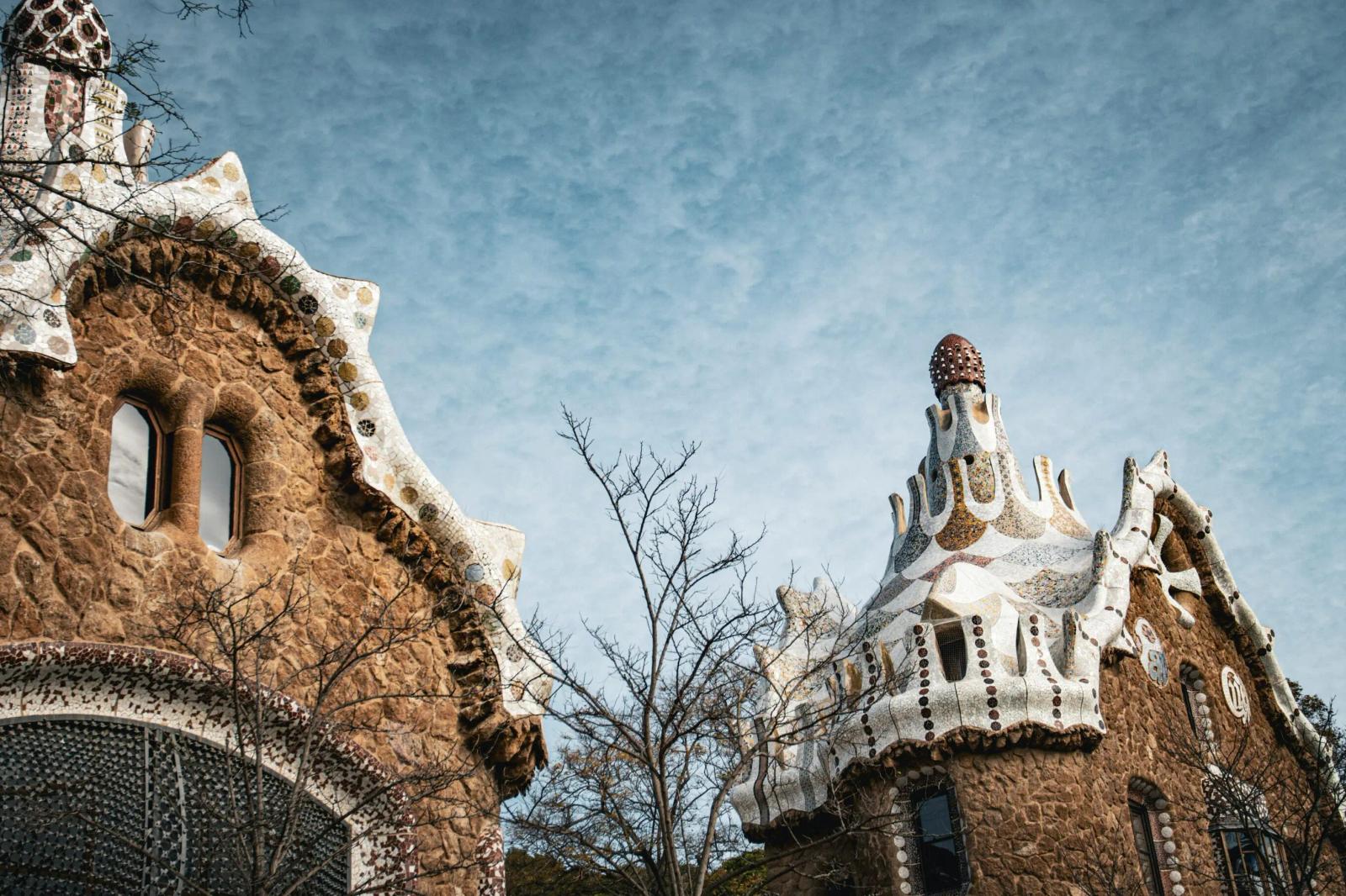 Vue sur les bâtiments emblématiques du parc Güell à Barcelone, conçus par l’architecte Antoni Gaudí, avec leurs toits ondulés recouverts de mosaïques colorées.